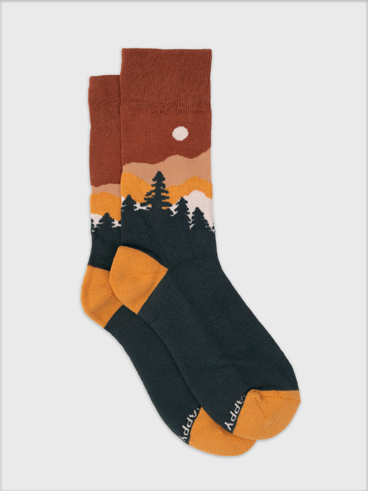 Highland socks featuring a sunset mountain landscape, green pine trees, and gold accents in soft organic cotton.