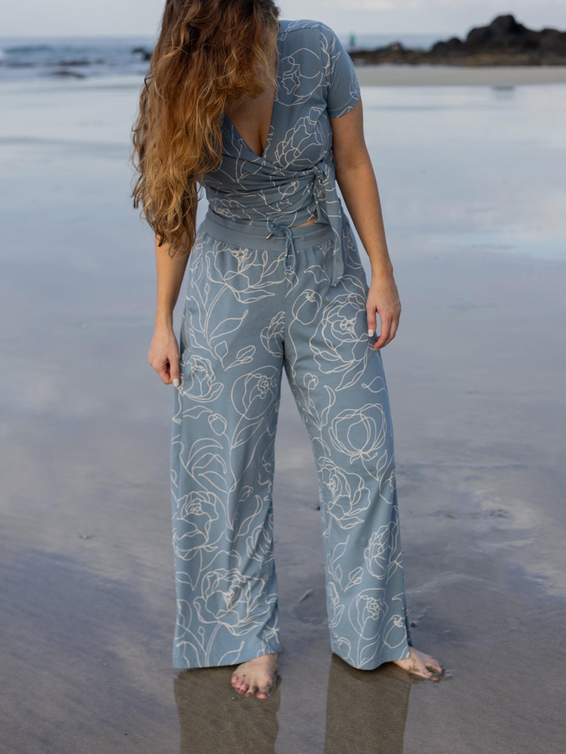 Woman in a blue organic cotton wrap crop top and matching wide-leg pants with white hand-drawn rose print.