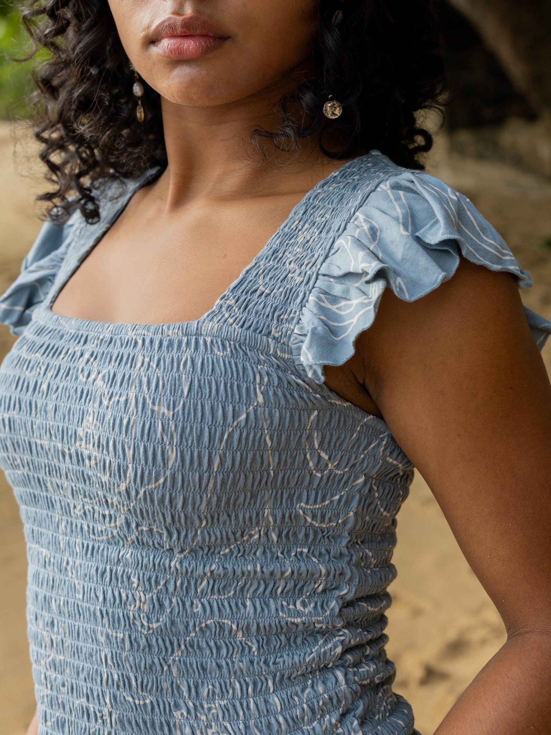 Smocked blue organic cotton top with white rose print, square neckline, and flutter cap sleeves.