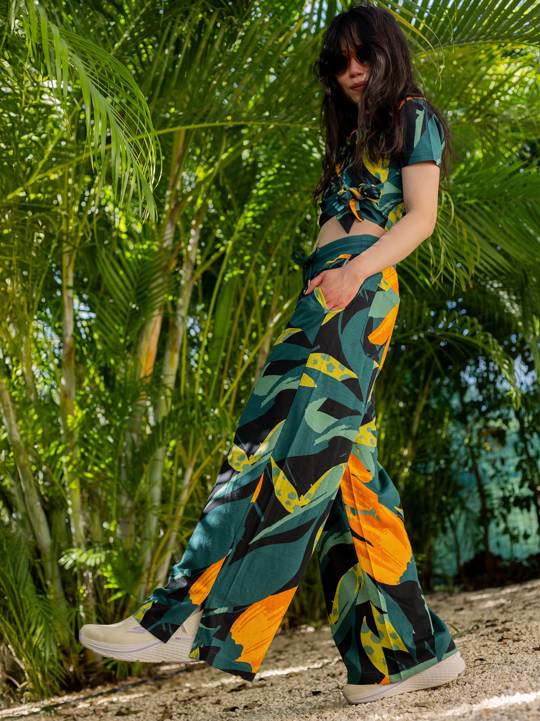 Woman in Hanalei Wide Leg Pants and matching top, featuring a vibrant green and orange tropical print.