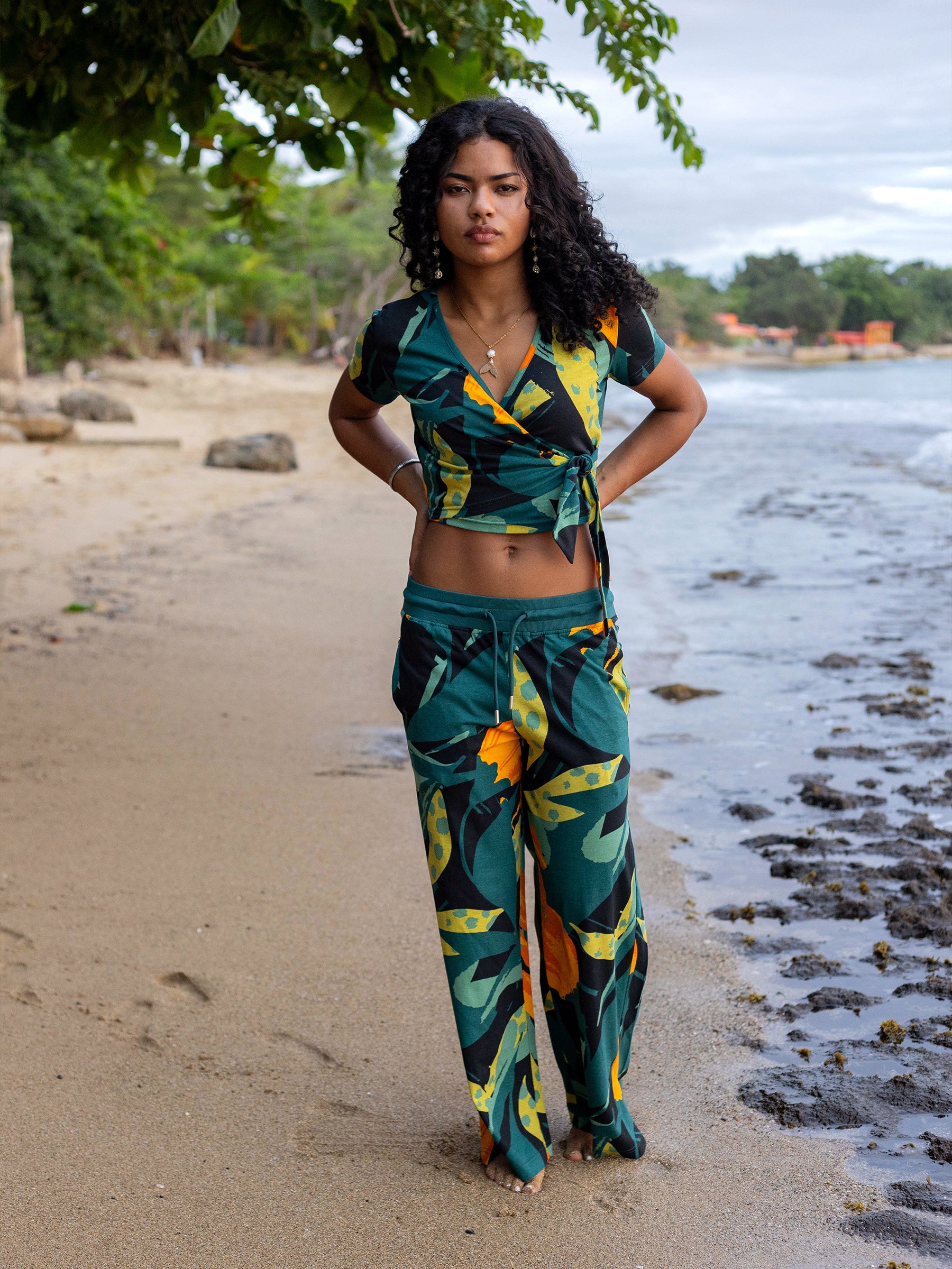 Woman in a green and gold floral organic cotton wrap crop top and matching pants on a beach.