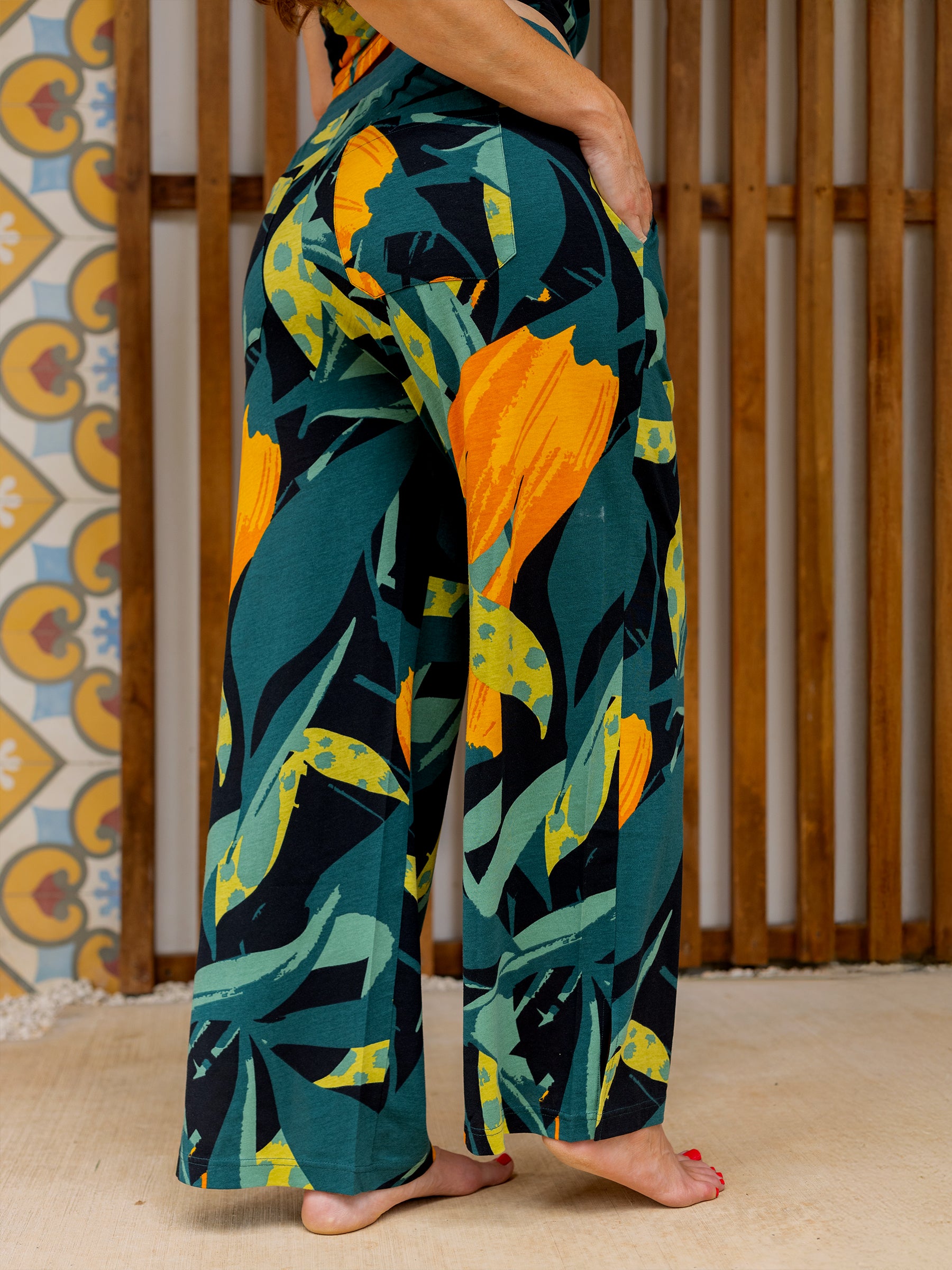 Woman wearing Hanalei wide-leg organic cotton pants with a vibrant green, black, and orange tropical print.