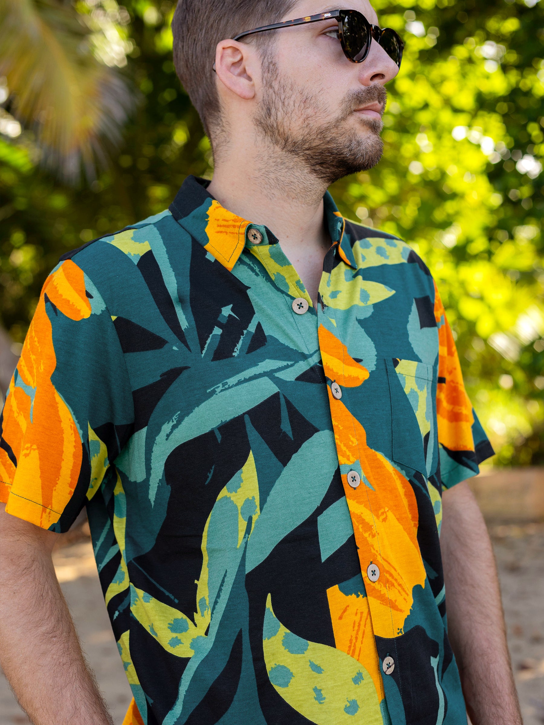 Man in a Rincon Shirt, a green, orange, and black tropical print organic cotton button-up with wooden buttons and a chest pocket.