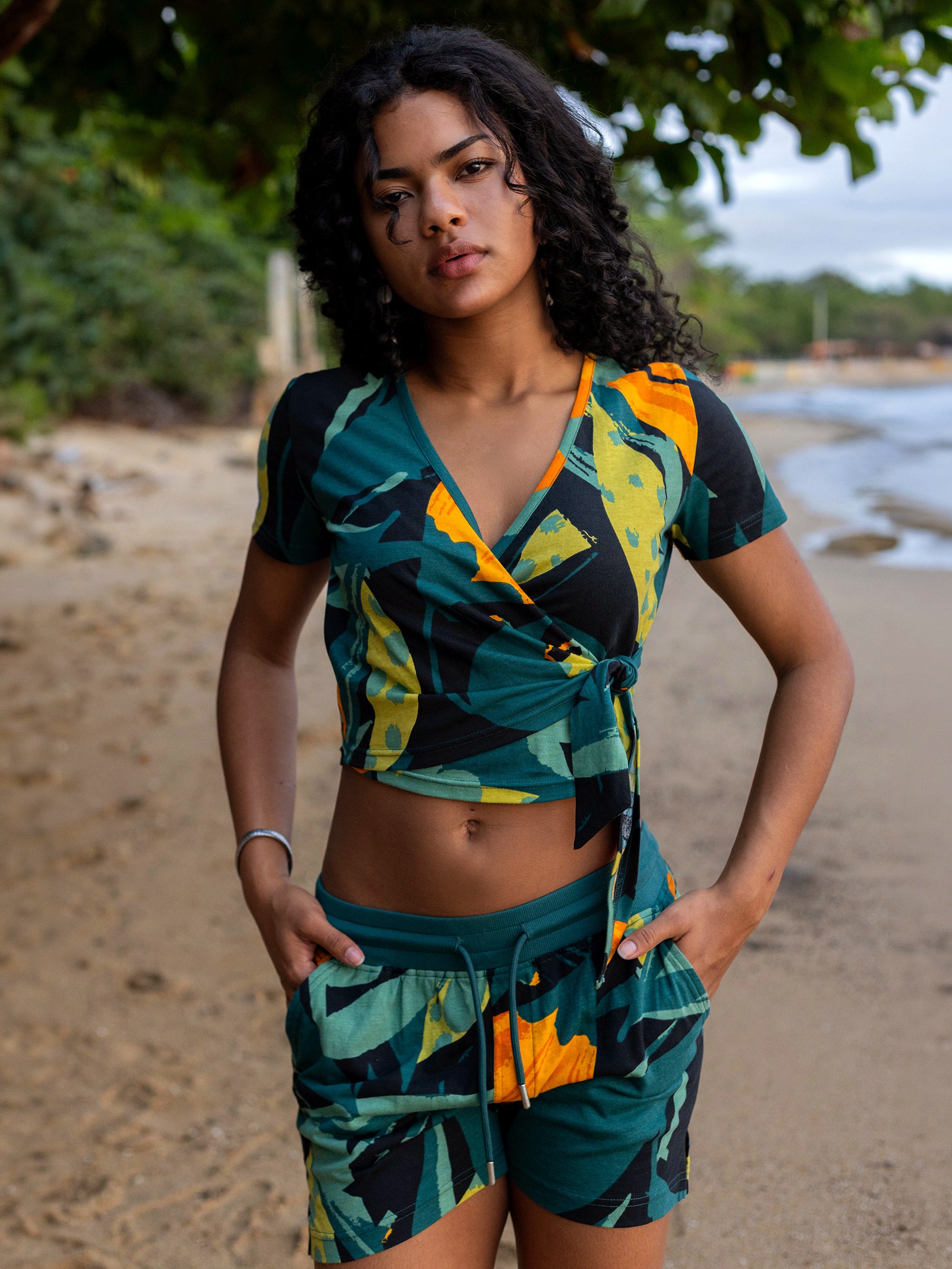 Woman in Hanalei Wrap Crop Top & matching shorts, featuring green, yellow, black tropical print.