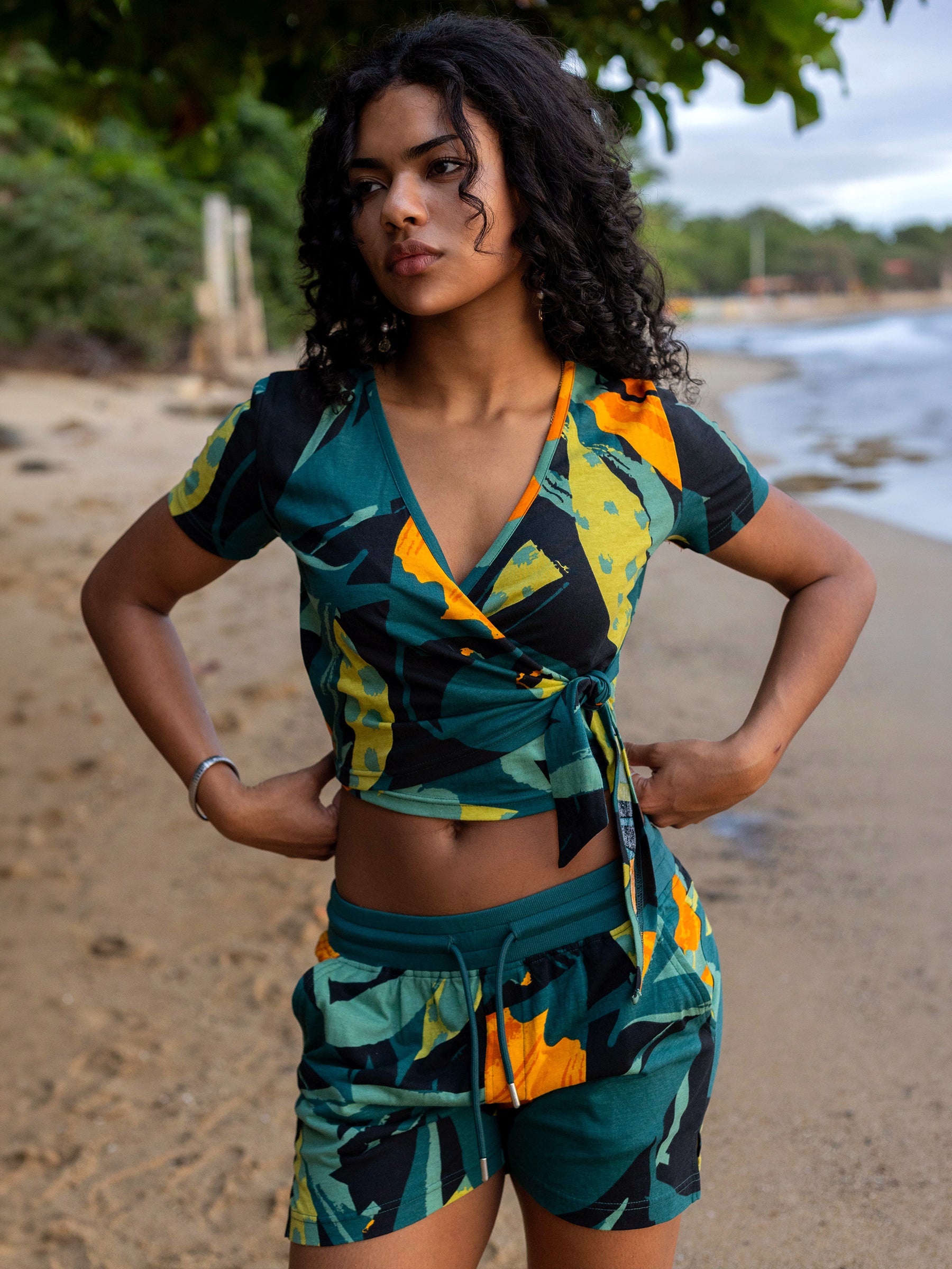 Woman on beach wearing Hanalei shorts and matching top with green, yellow, and black abstract print.