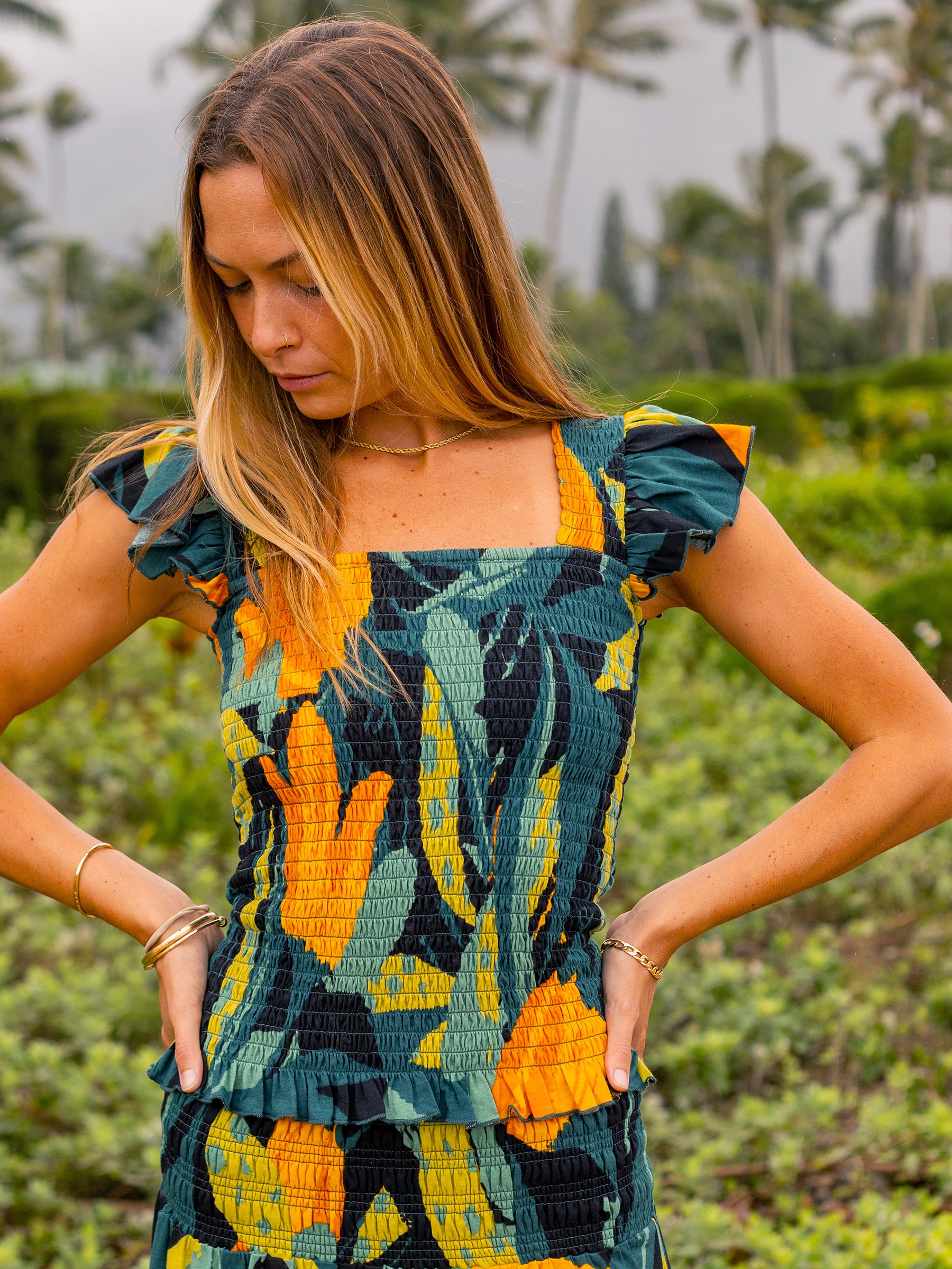 Woman in a Hanalei smocked top with square neckline, flutter sleeves, and ruffled hem in a tropical print.