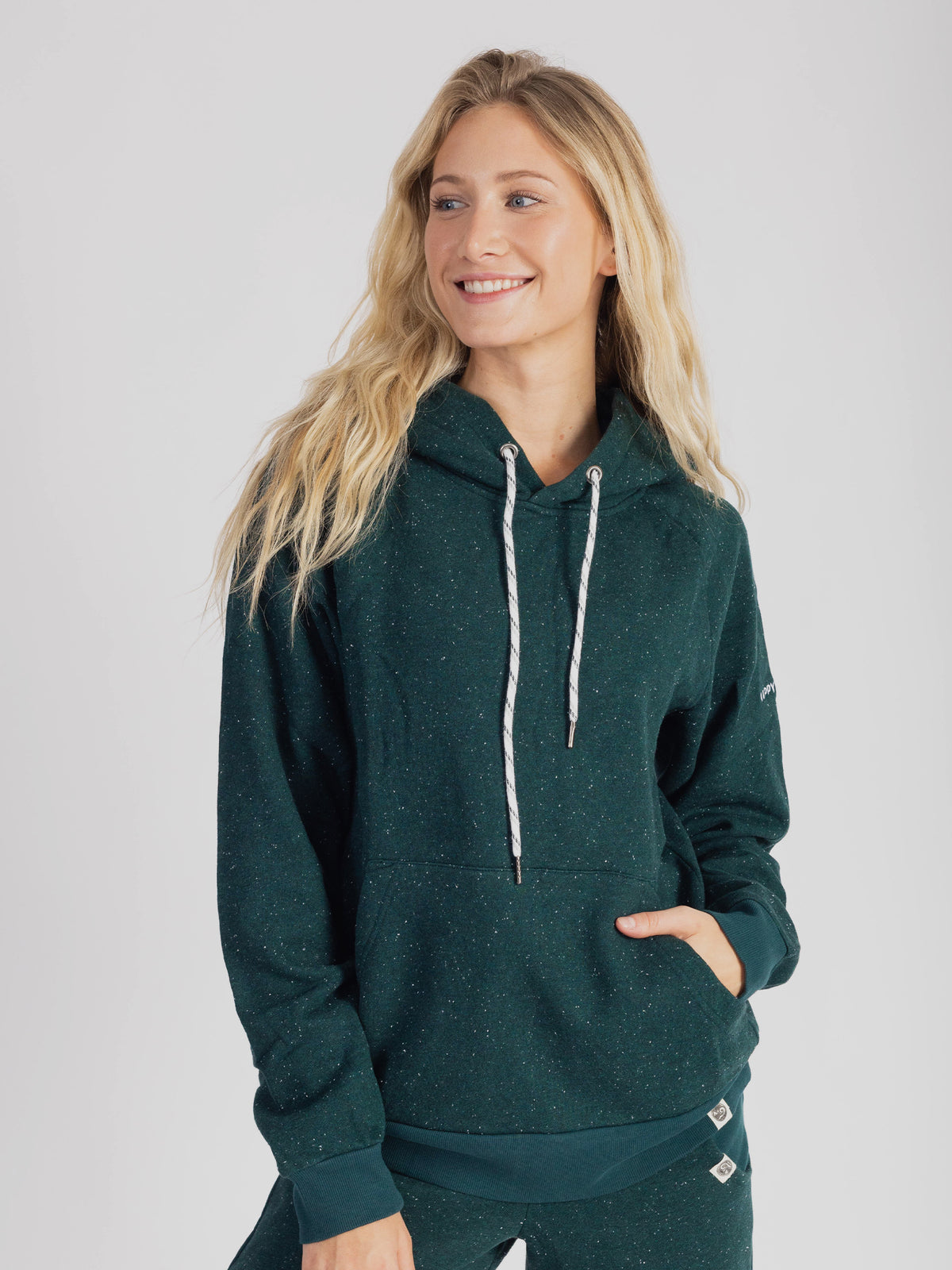 Smiling model wearing the speckled Monstera teal organic cotton hoodie, hand in pocket