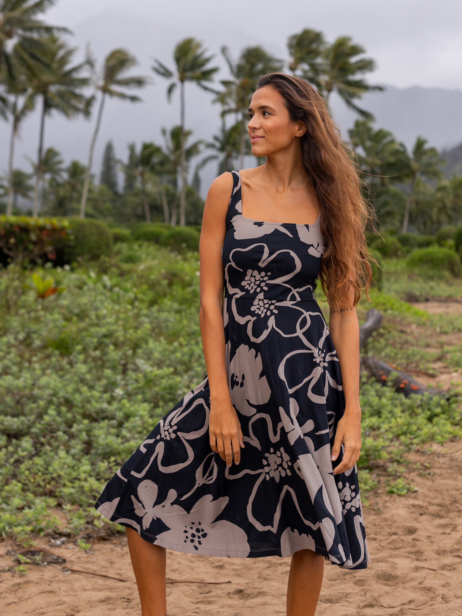 Woman in Lily Dress, a black organic cotton midi with taupe moonflower print, square neckline, and wide straps.