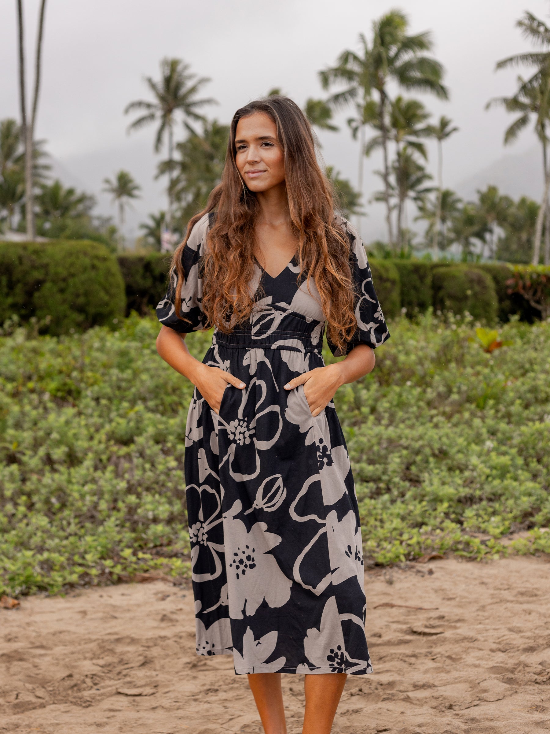 Woman in a black Ophelia midi dress with taupe moonflower print, V-neck, puffed sleeves, and smocked waist.