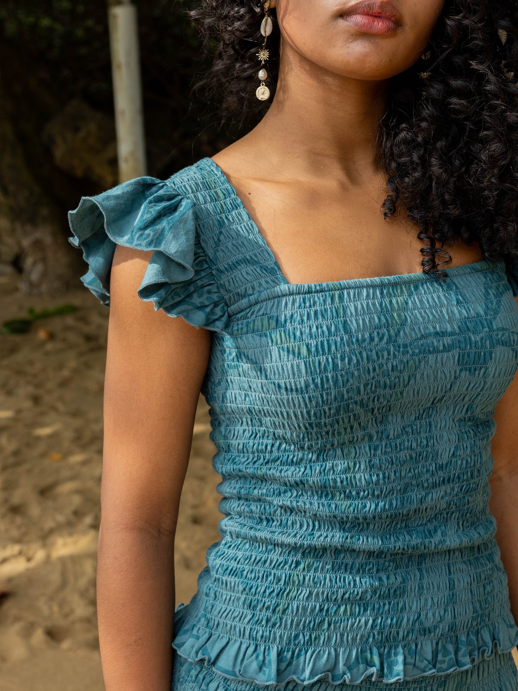 Teal smocked organic cotton top with square neckline, flutter cap sleeves, and ruffled hem.
