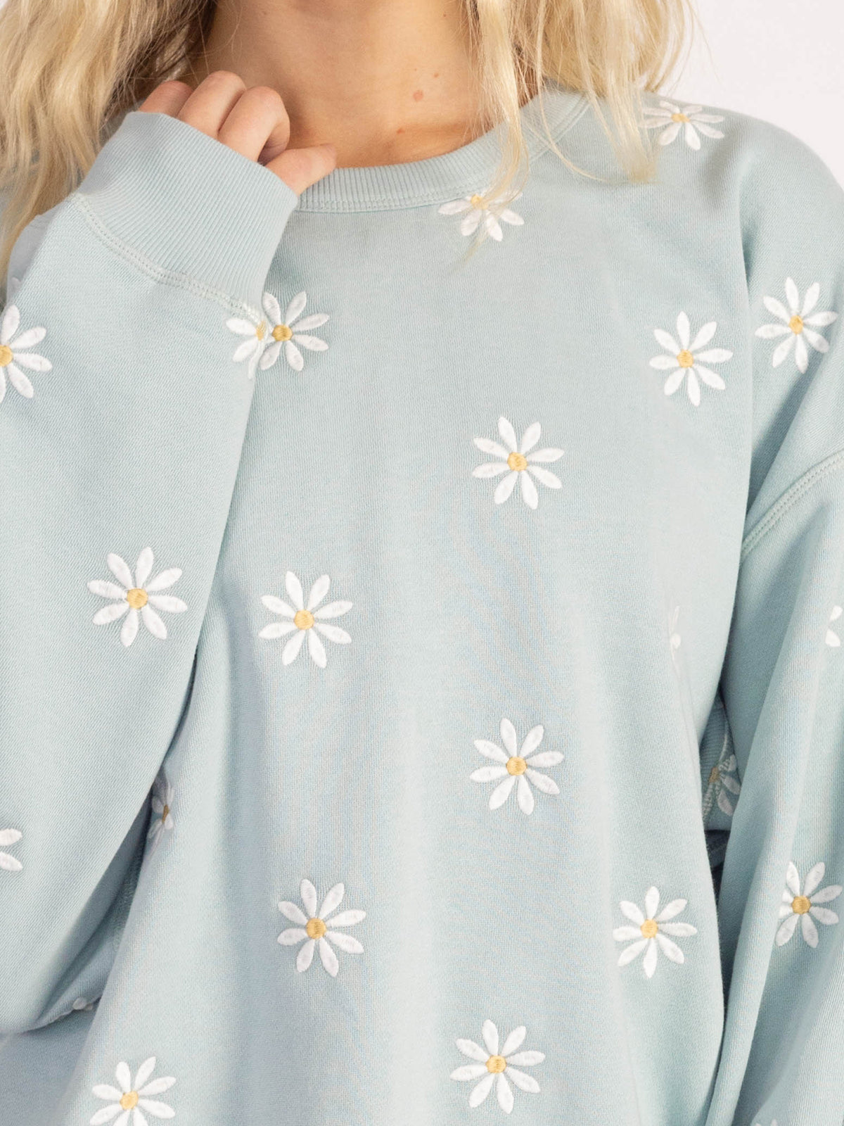 Close-up of white daisy embroidery on the light blue Daisies organic cotton sweatshirt