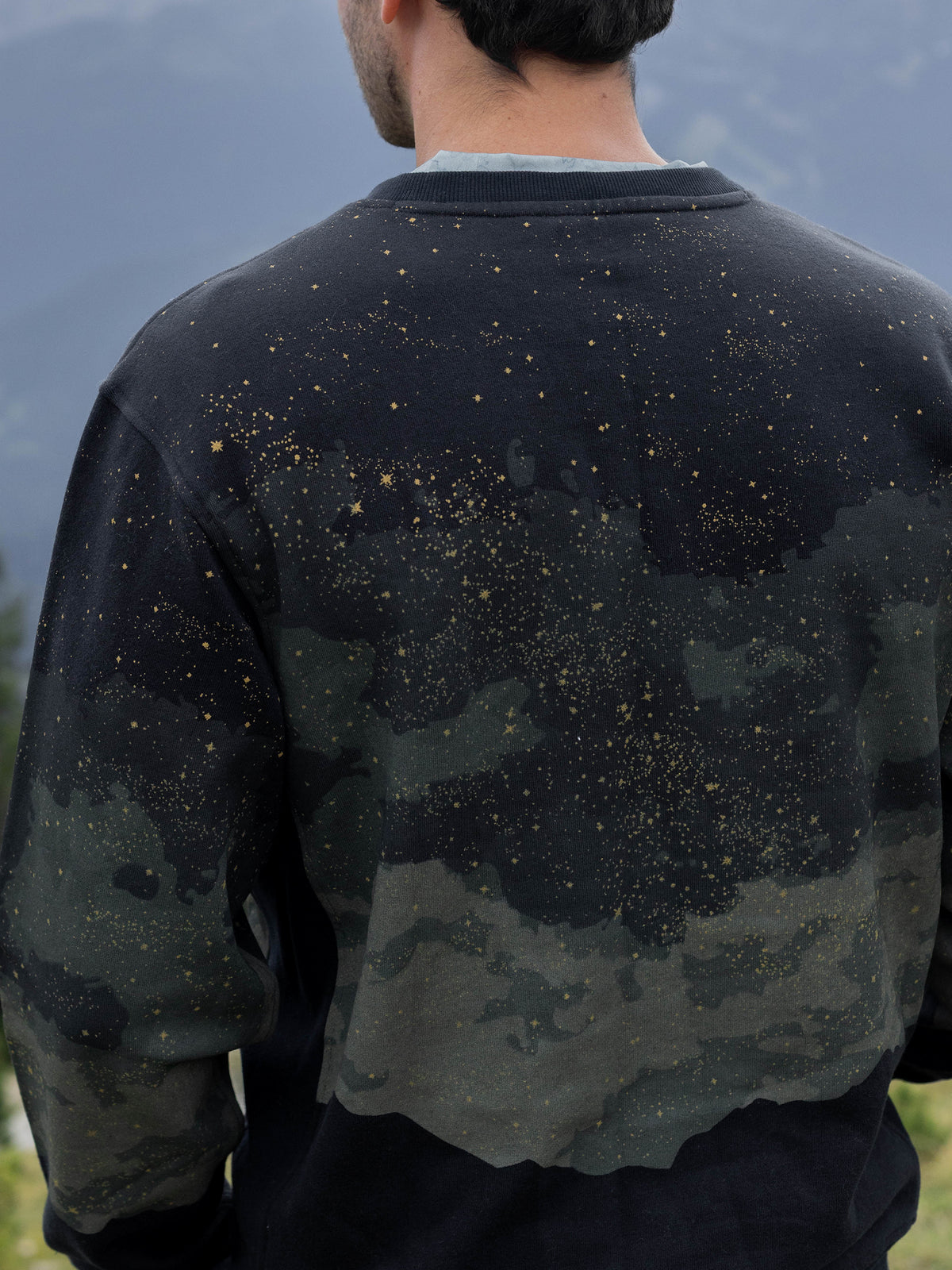 Close-up of gold stars and clouds on the back of the black Embercrest organic cotton sweatshirt