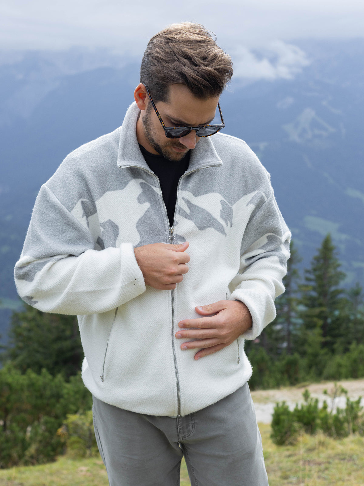 Model zipping up the white Altitude organic cotton sherpa jacket on a mountainside