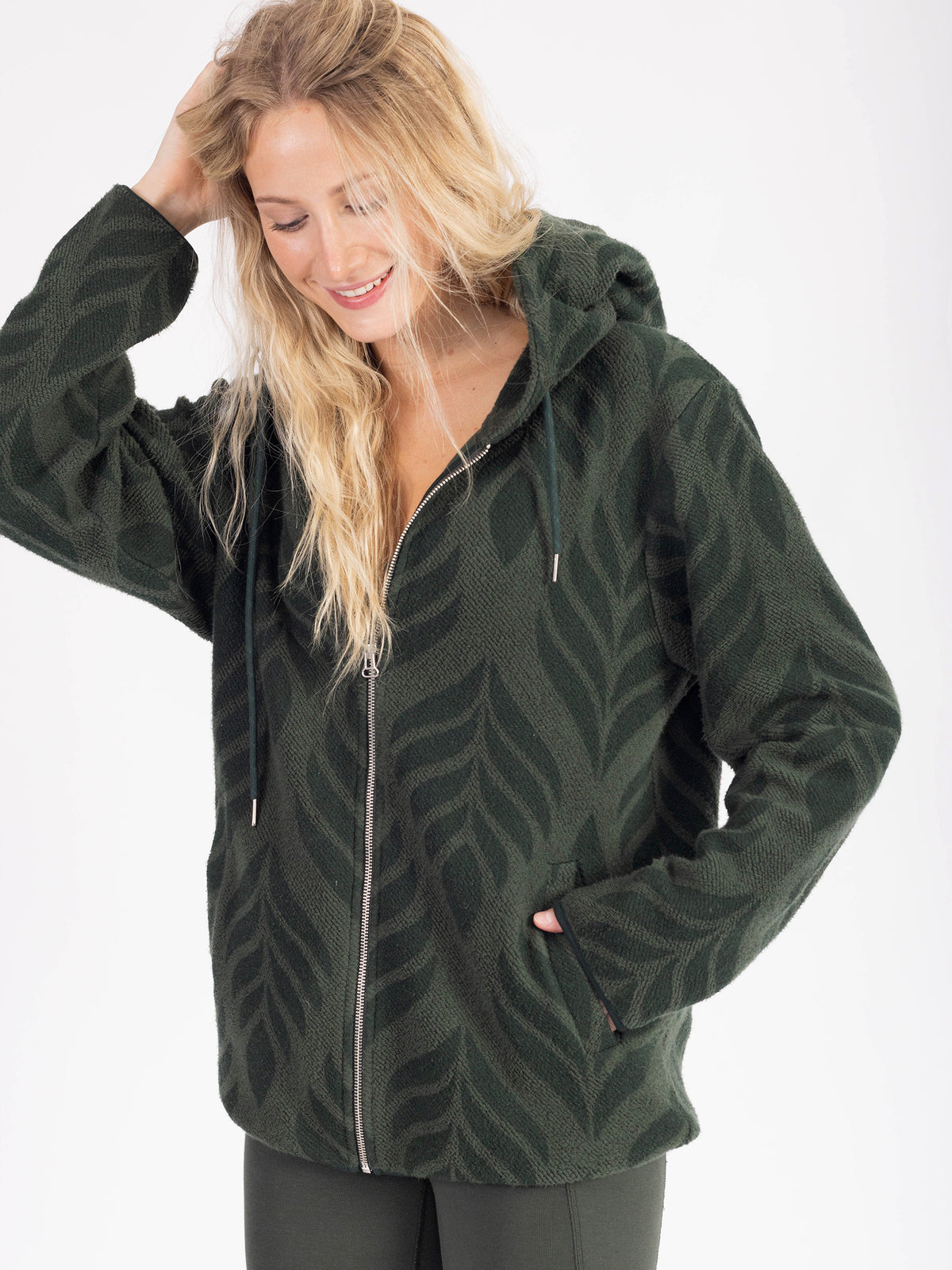Model wearing the forest green Verdant organic cotton sherpa zip hoodie unzipped over leggings