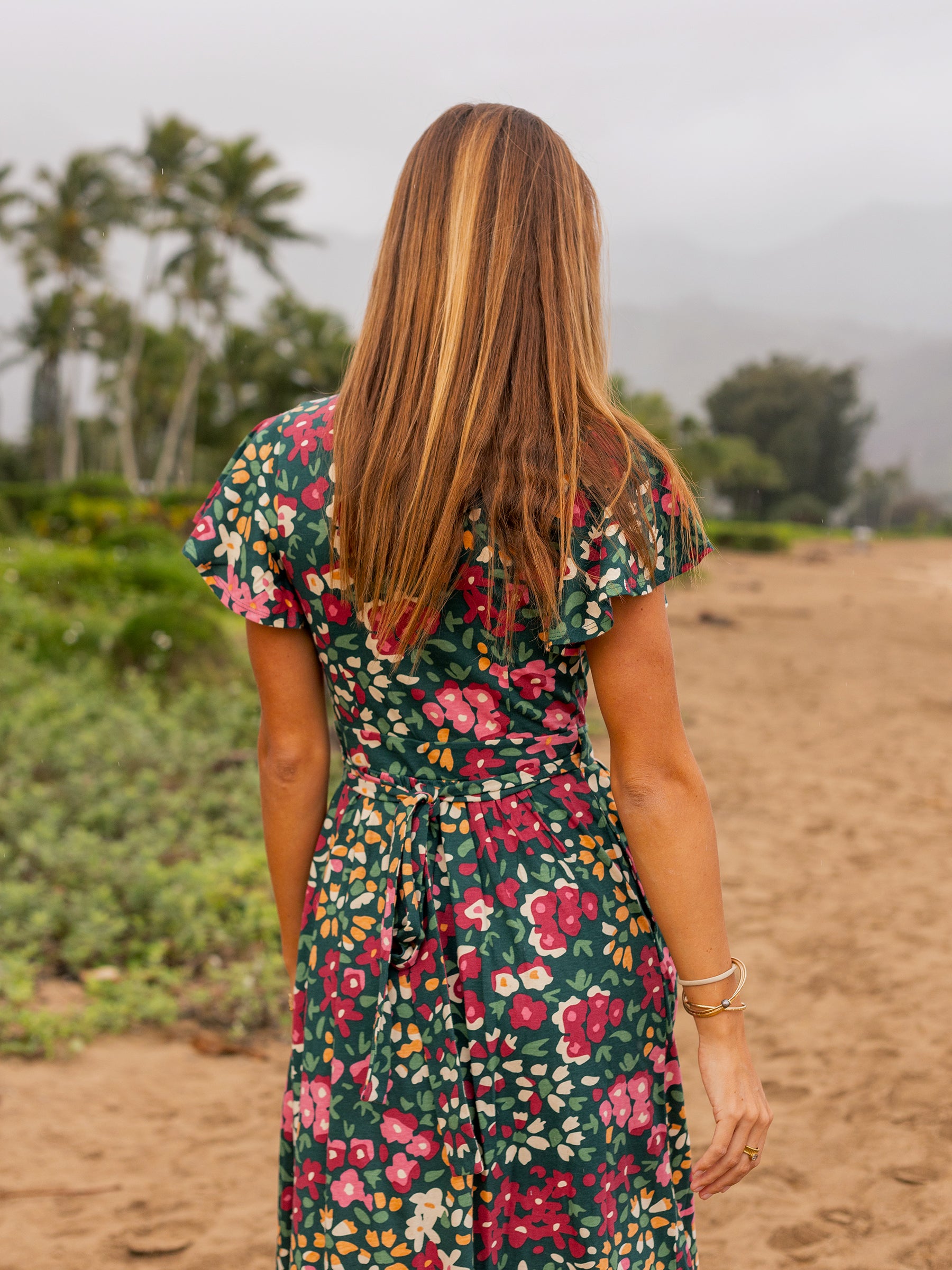 Woman from behind wearing a green Isla Wildflowers maxi wrap dress with flutter sleeves and ribbon tie.
