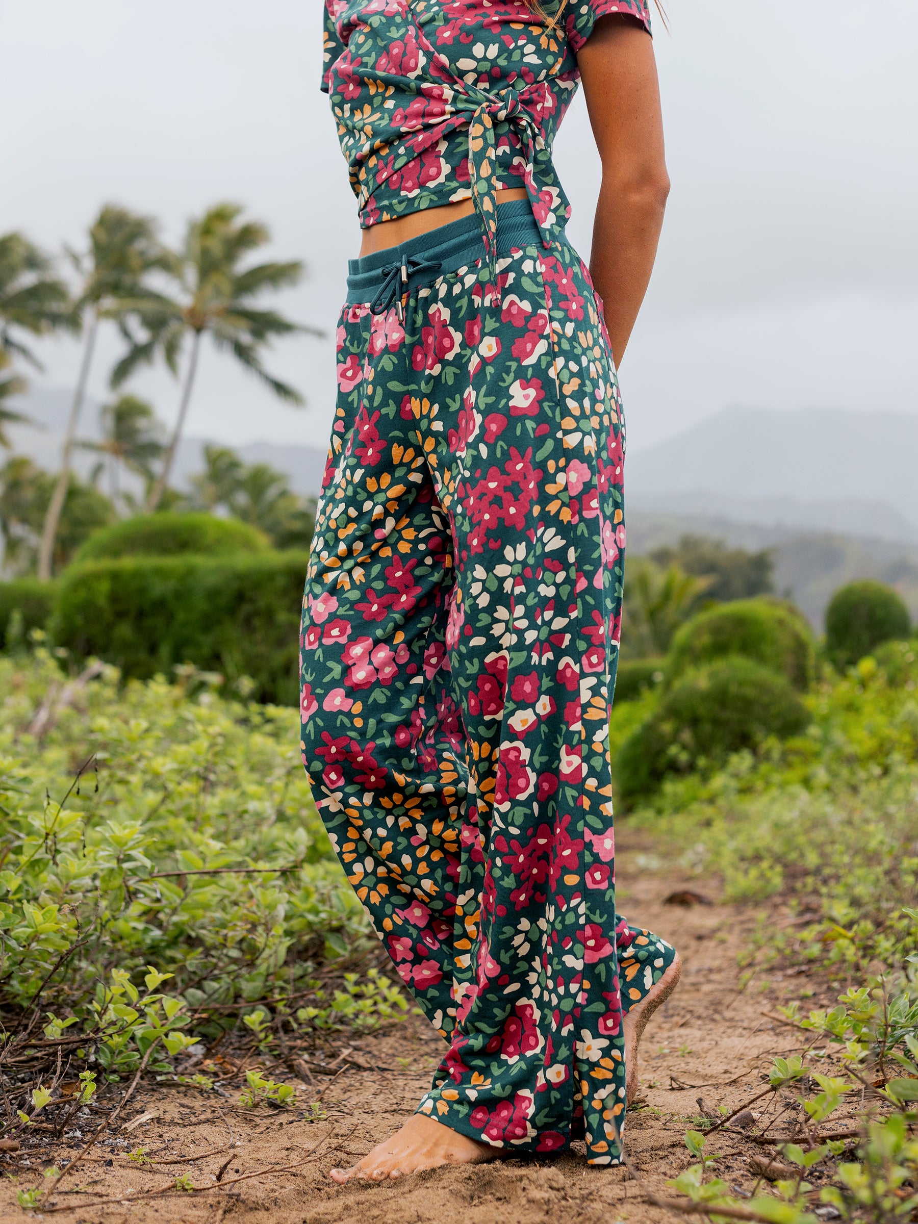 Model wearing Wildflowers wide-leg organic cotton pants with a vibrant floral print and side slits.