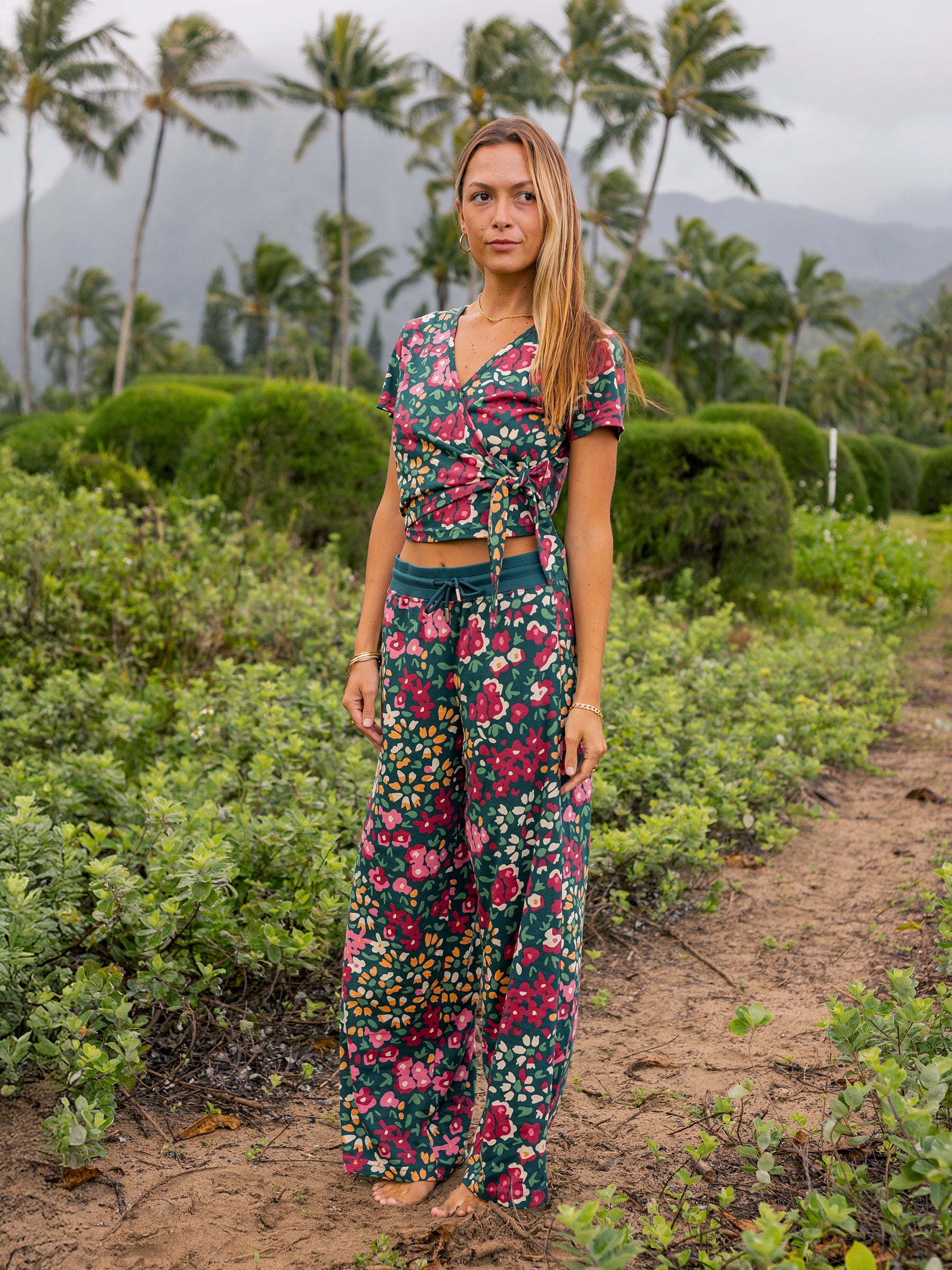 Woman in a green wide-leg organic cotton pants and matching floral wrap top, standing outdoors.