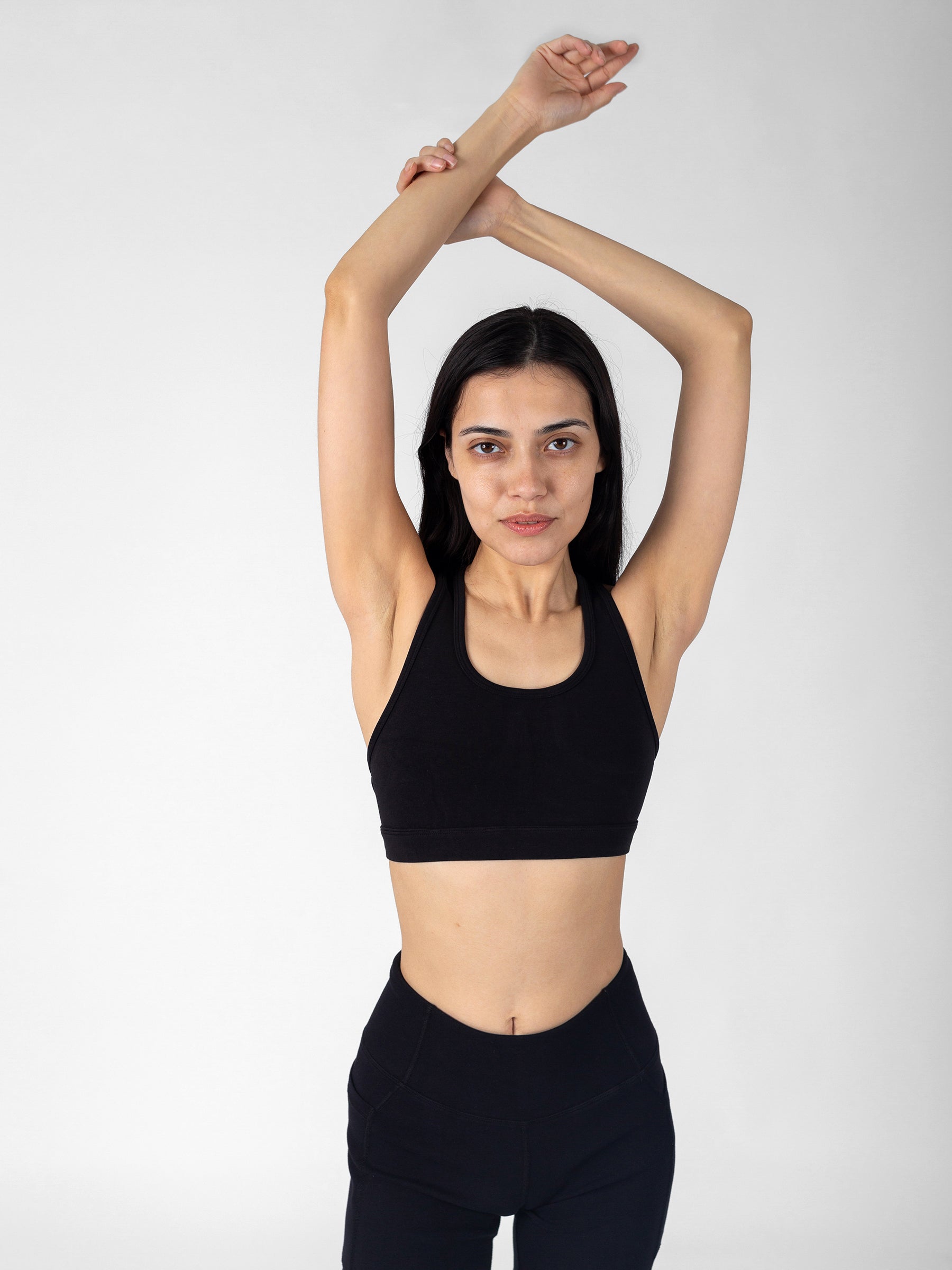 Front view of Eclipse black PlantTec sports bra, arms overhead, racerback construction, GOTS-certified organic