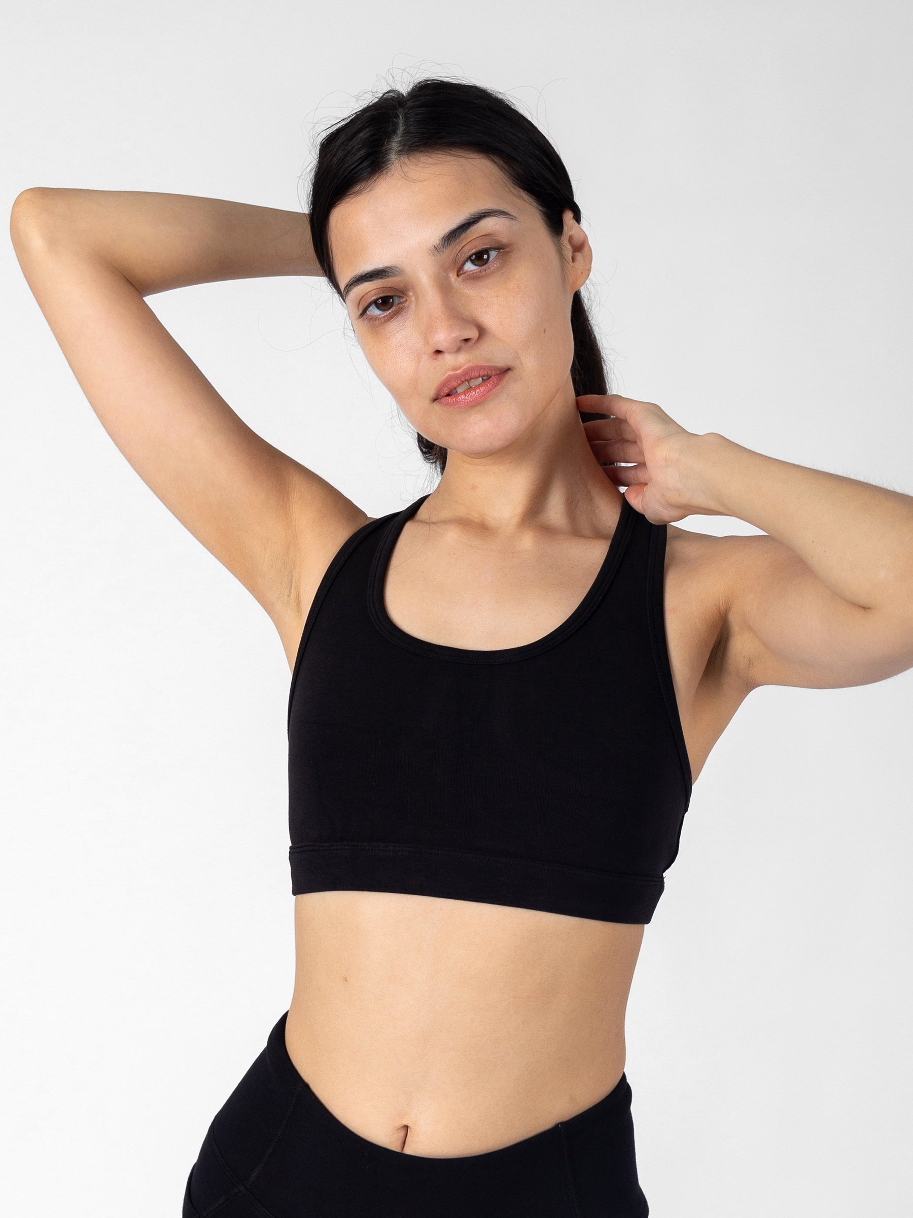 Front view, Eclipse black sports bra, arm raised showing racerback strap detail, scoop neck, organic cotton