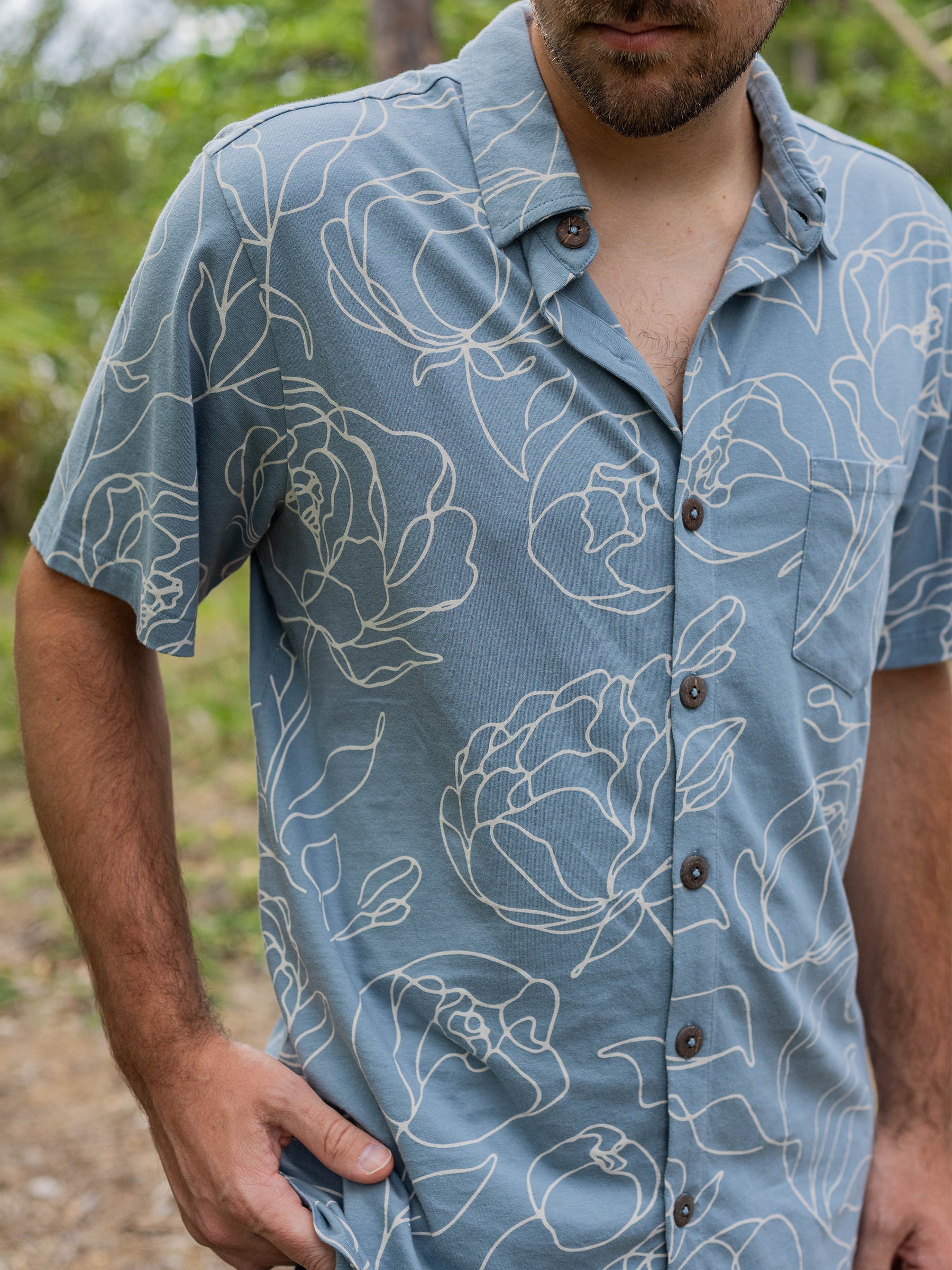 Men's Rincon Shirt in Garden Rose, a light blue organic cotton jersey with white hand-drawn roses and wooden buttons.