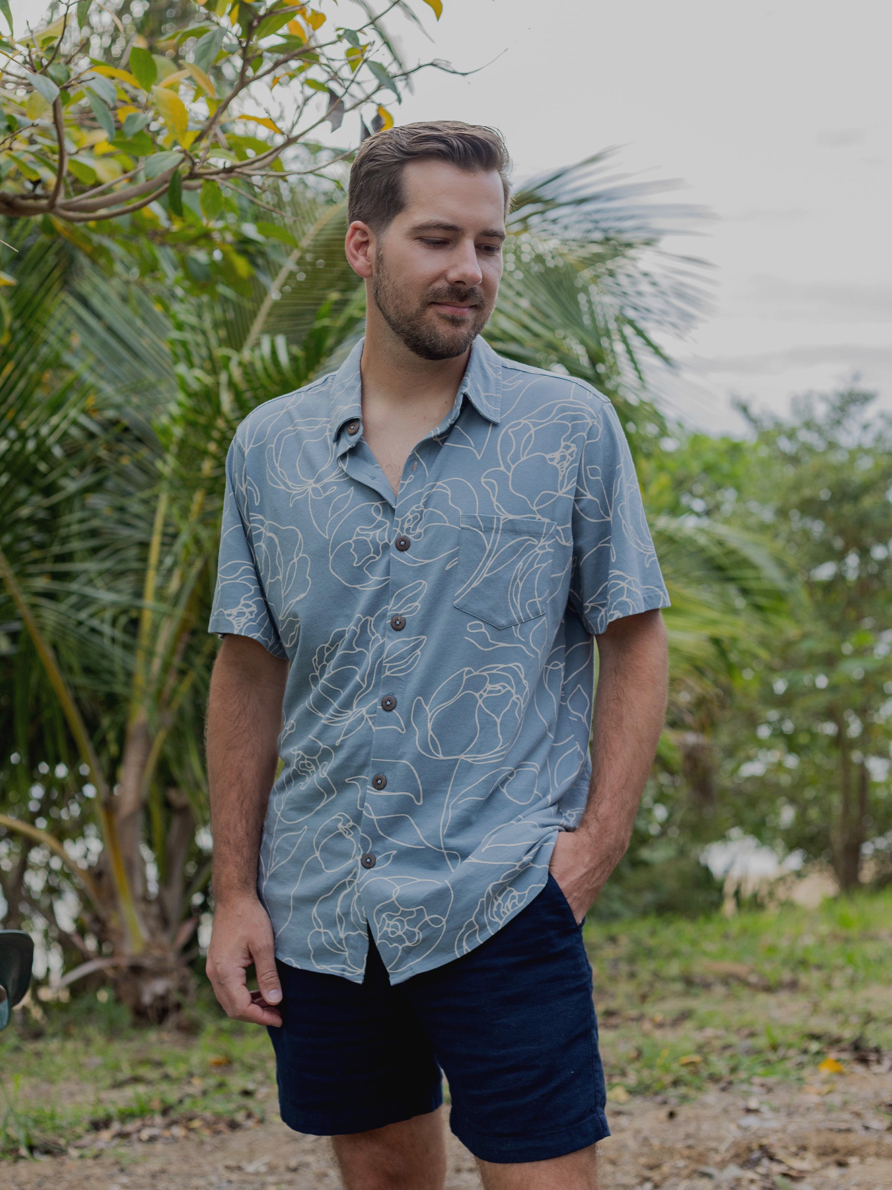 Men's Rincon Shirt in Garden Rose: light blue organic cotton jersey with white hand-drawn roses, classic collar, and wooden buttons.