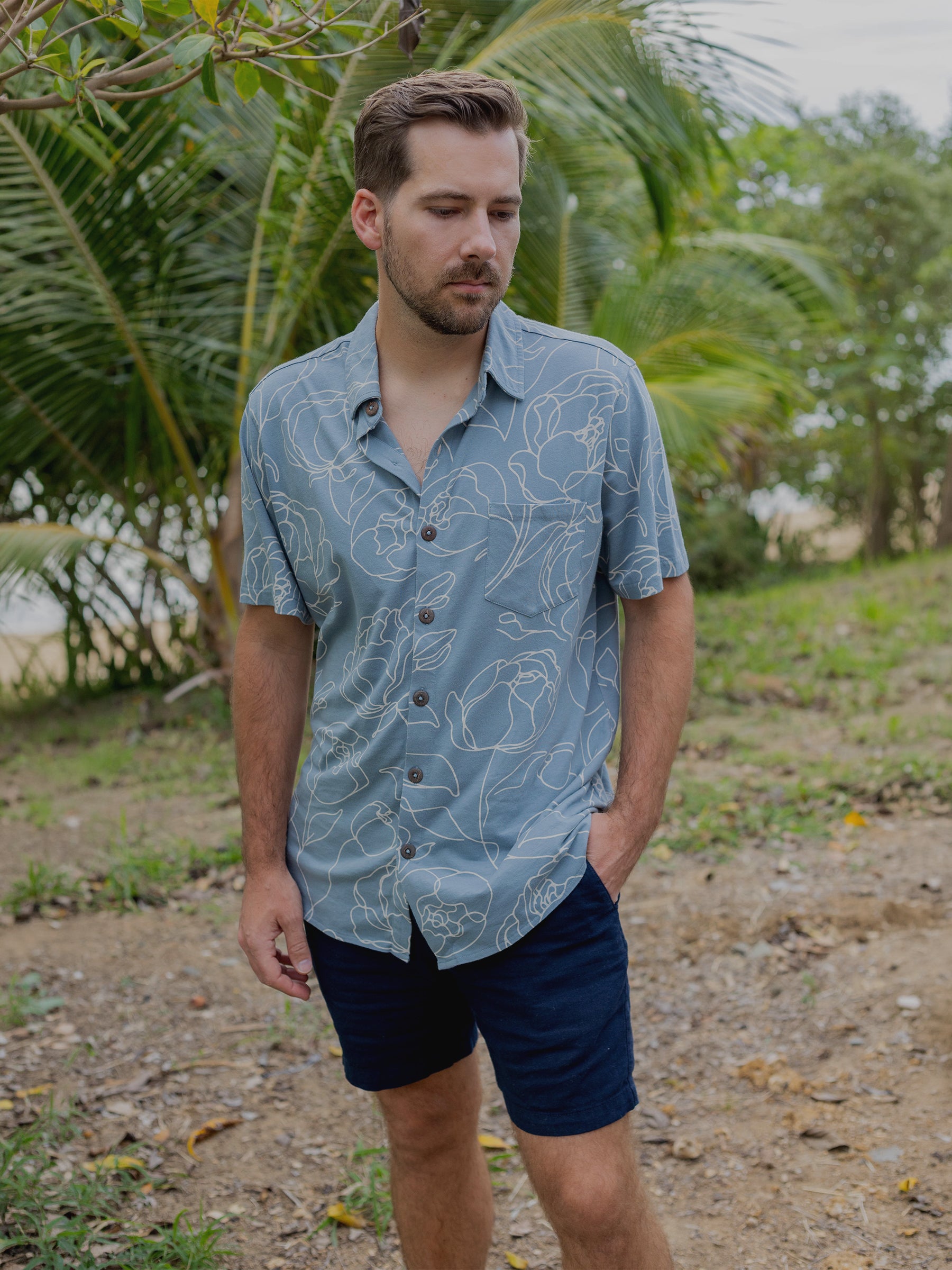 Man in a blue organic cotton Rincon Shirt with white hand-drawn roses, wooden buttons, and a chest pocket.