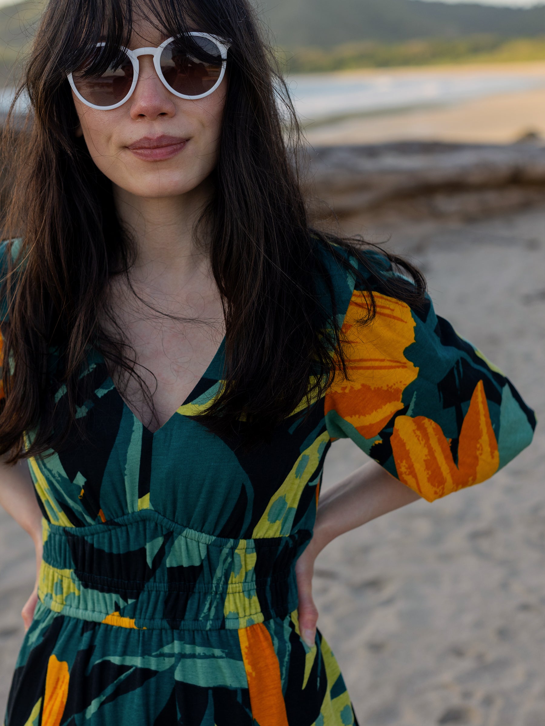 Woman in Ophelia Dress: green, black, and orange floral print, V-neck, puffed sleeves, smocked waist.