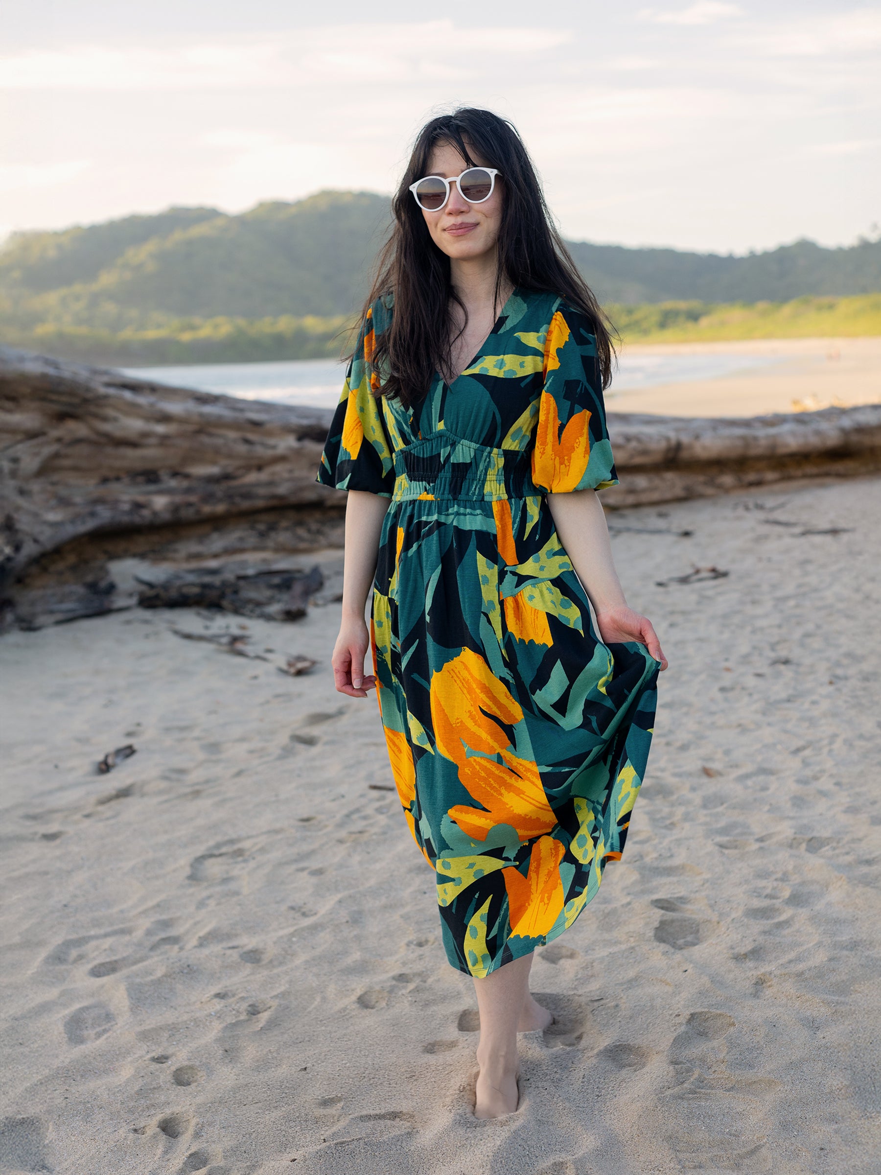 Woman in Ophelia Dress: green, orange, and yellow floral midi dress with V-neck, puffed sleeves, and smocked waist.