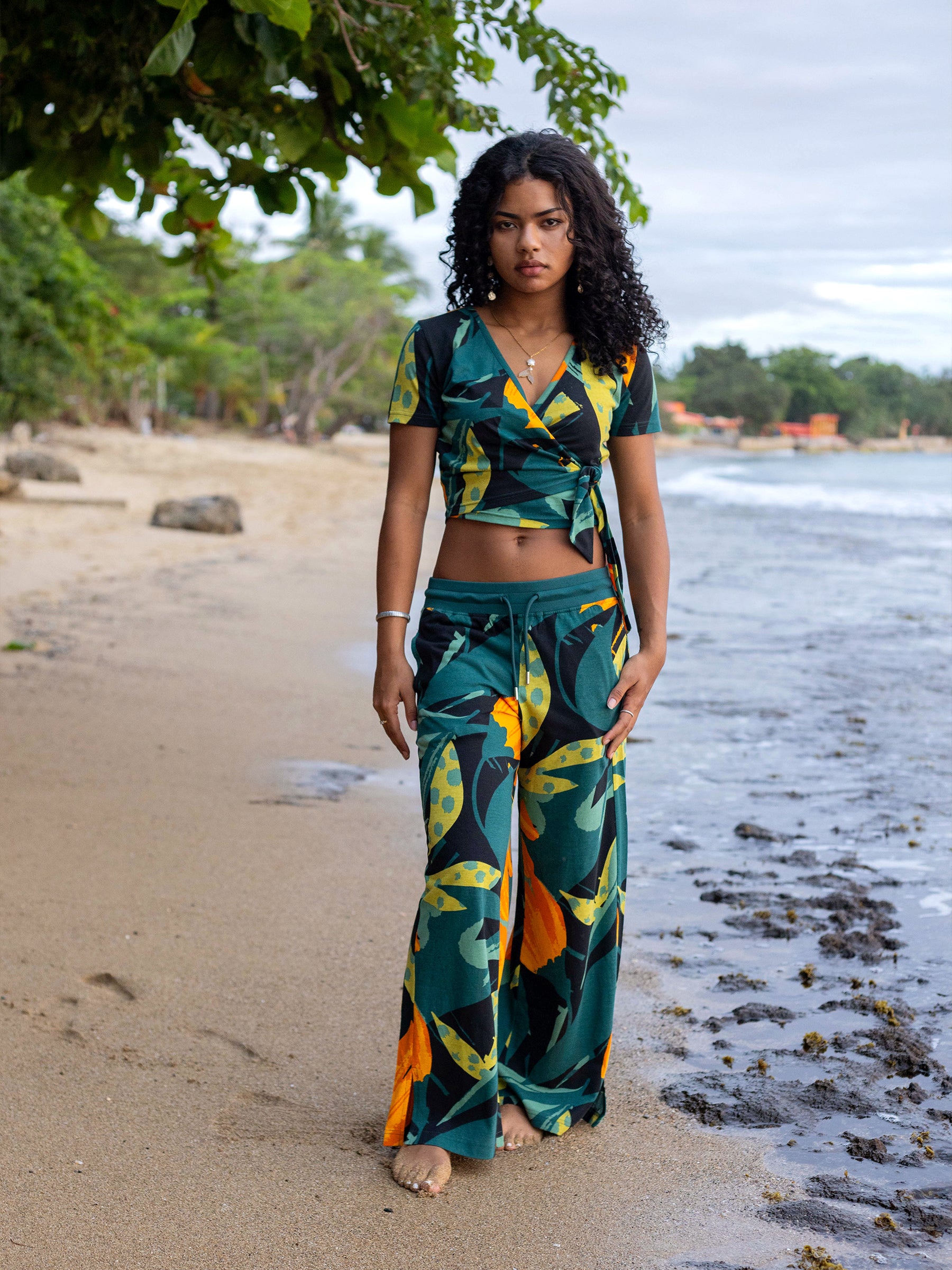 Woman on beach wearing Hanalei wide-leg organic cotton pants and matching crop top with green, yellow, and black floral print.