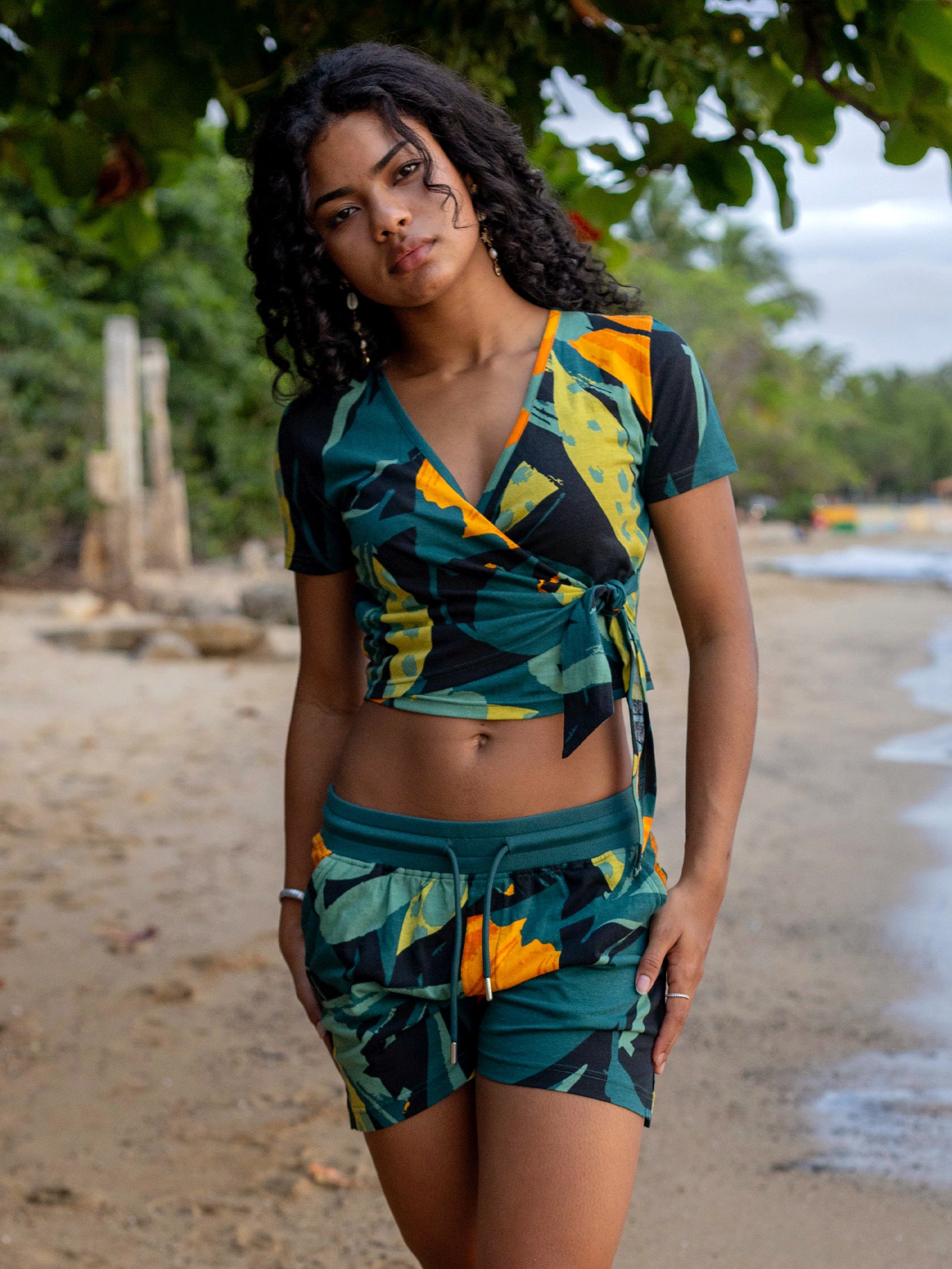 Woman wearing Hanalei shorts and matching top in a green, yellow, and black tropical print.