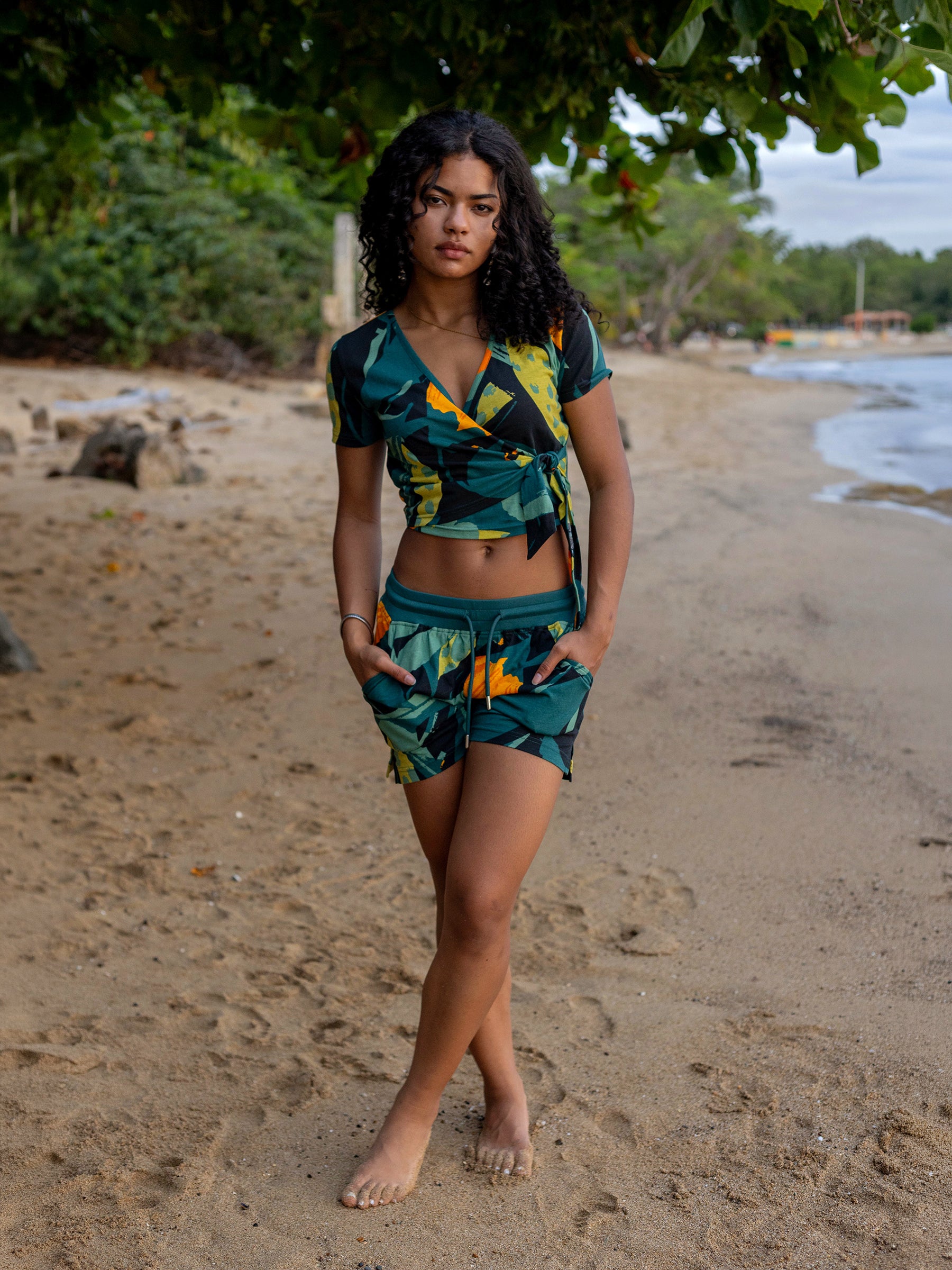 Woman on beach wearing Hanalei shorts and matching top with green and golden floral pattern.