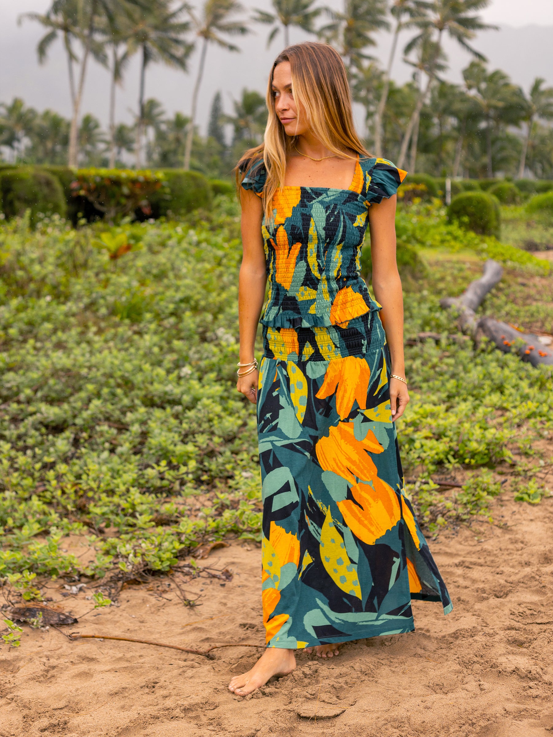 Woman in a Hanalei smocked maxi skirt and matching top with a tropical green and golden floral print.