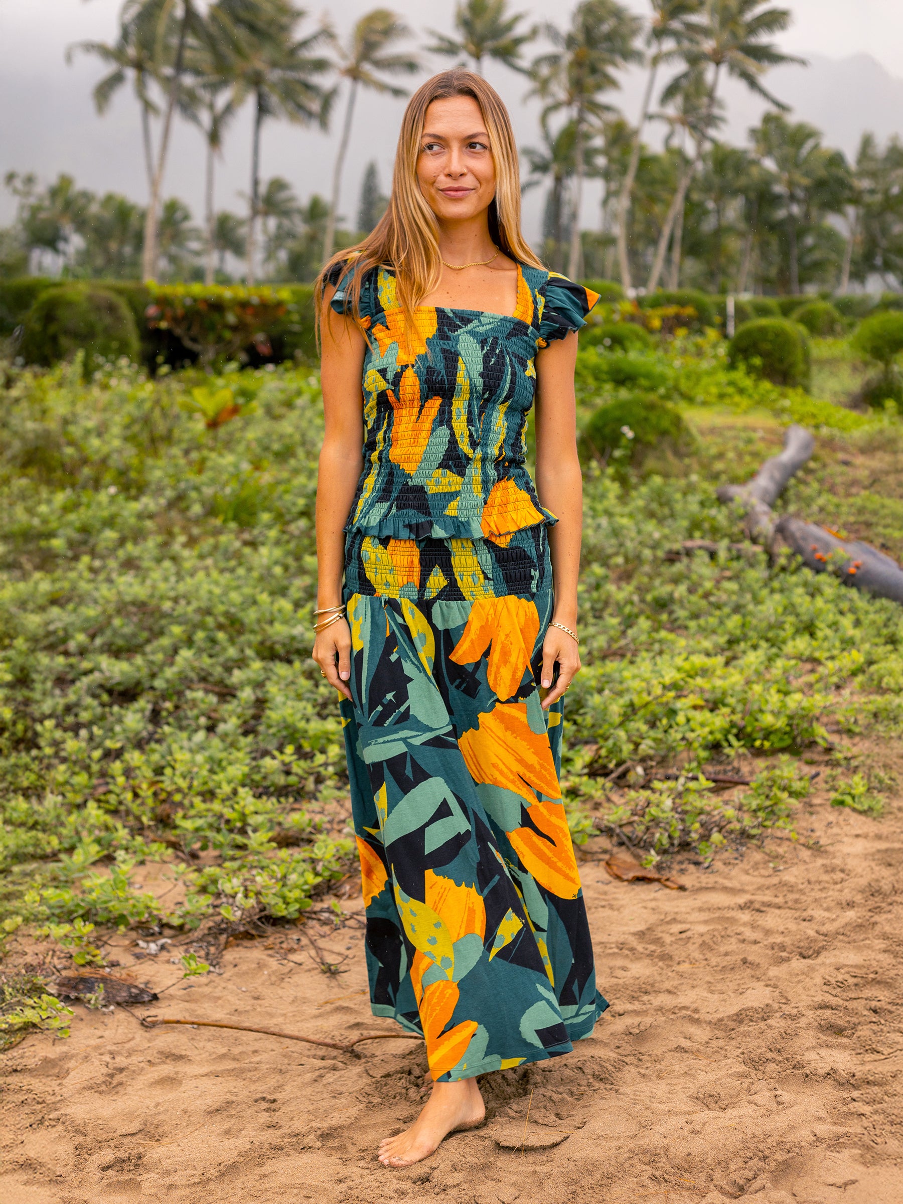 Woman in a Hanalei smocked maxi skirt and top with lush green and golden floral print.