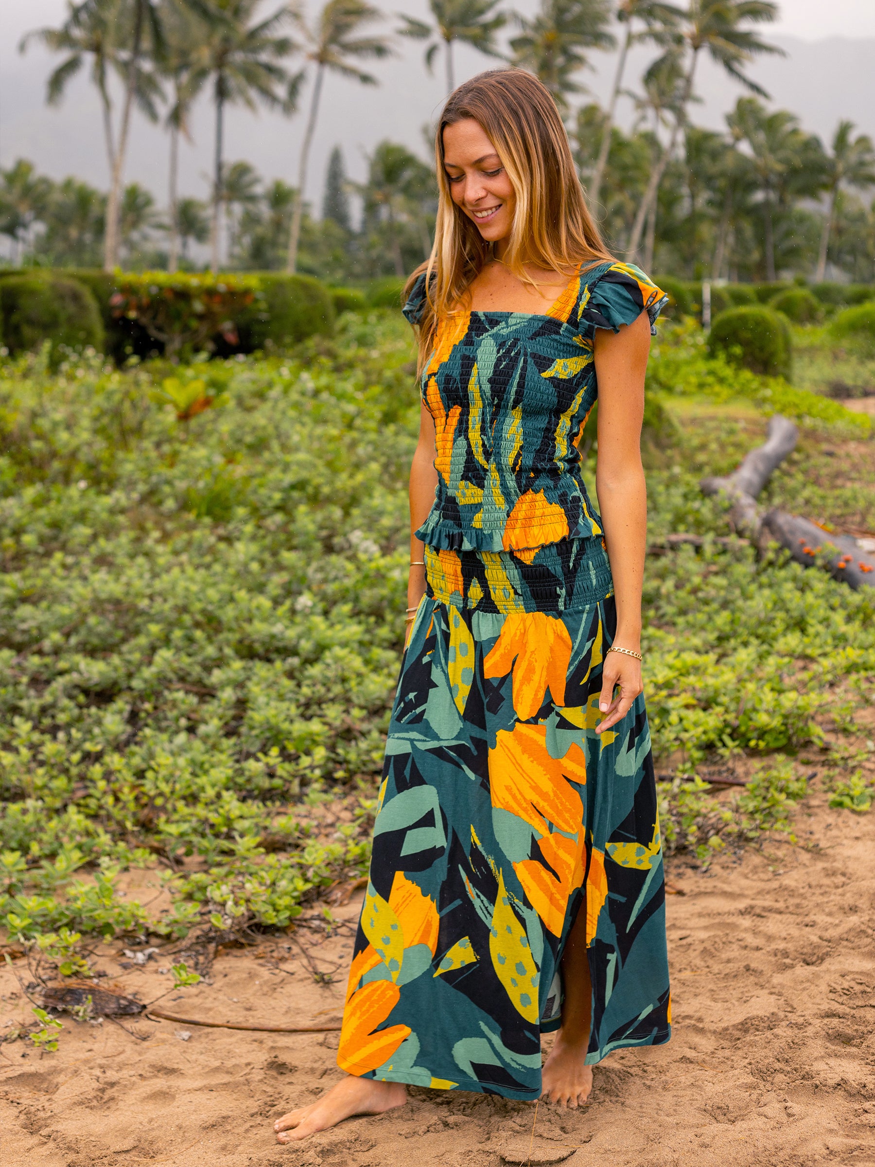 Woman in a Hanalei smocked top and matching maxi skirt, featuring lush green and golden floral print.