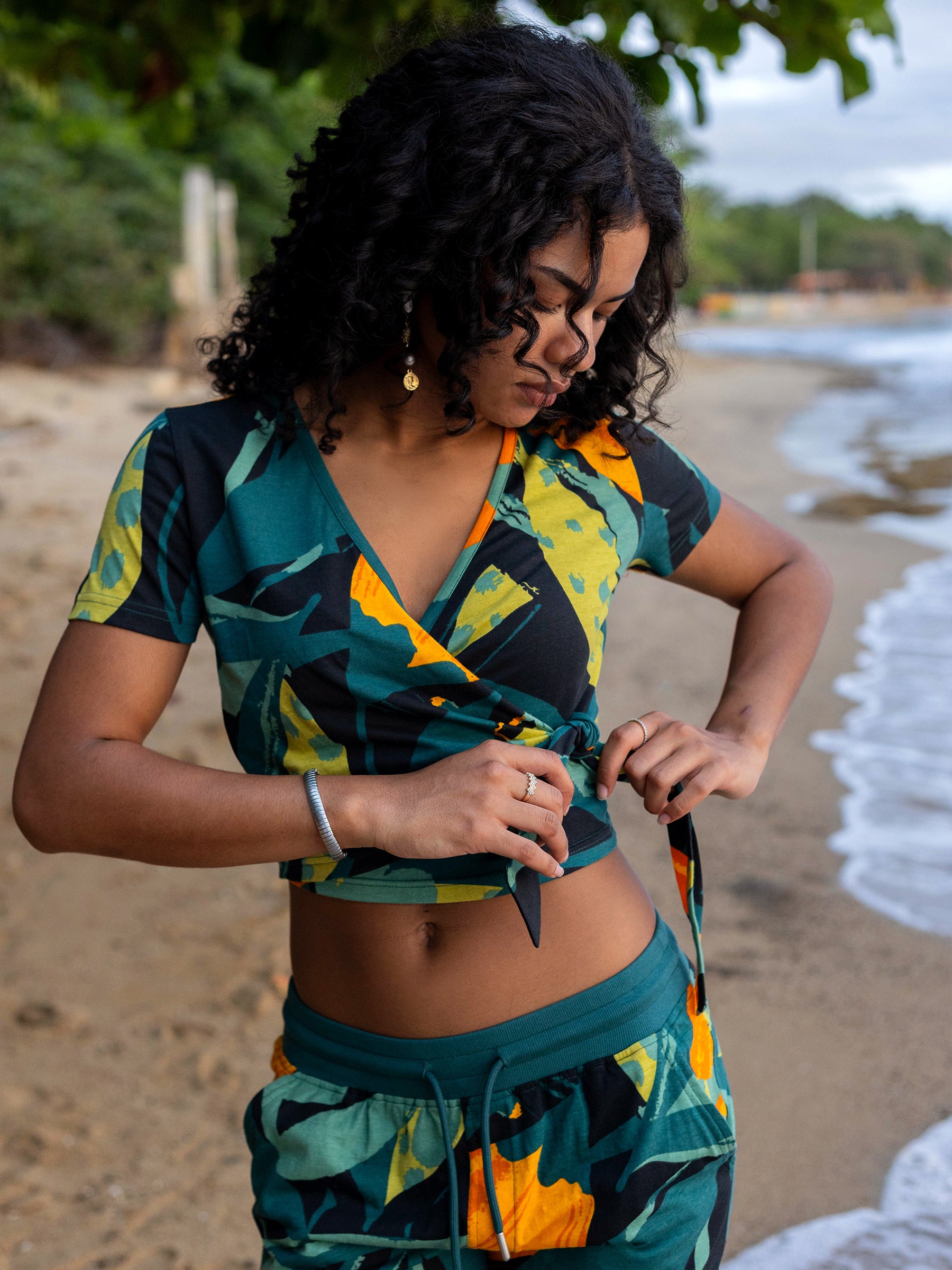 Woman in a Hanalei Wrap Crop Top with lush green, golden bloom print, tying the waist.
