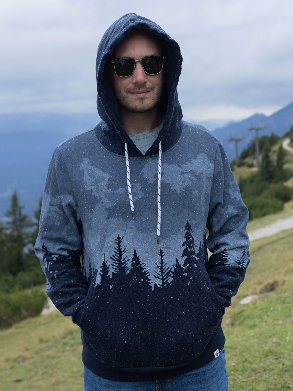 Model wearing the Stardust organic cotton hoodie with the hood up on a mountainside