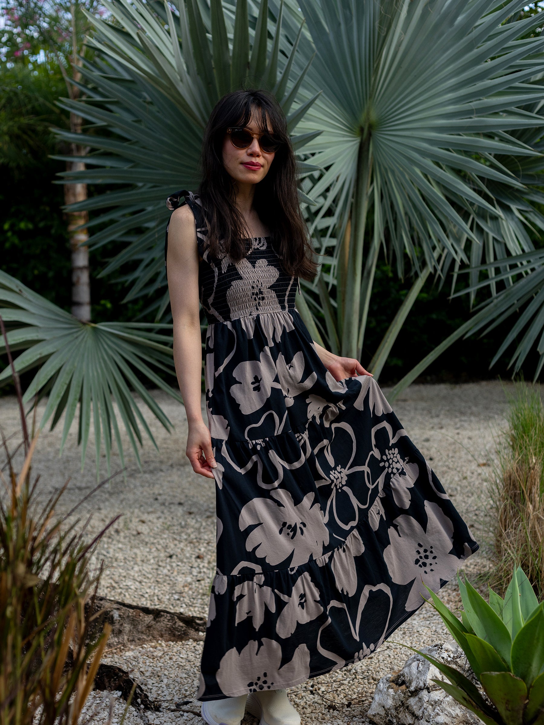 Woman in Evie Smocked Dress, black with taupe moonflower print, tiered maxi skirt, and smocked bodice.