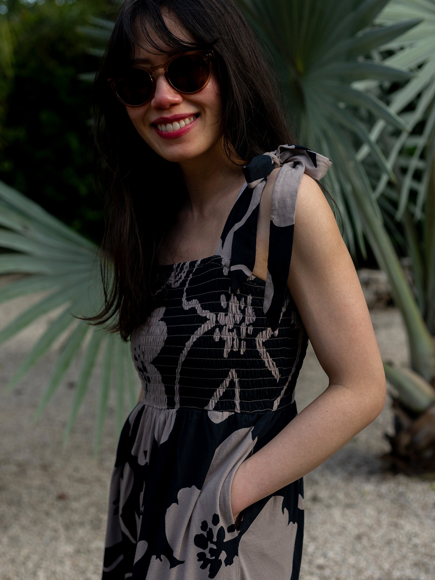 Woman in Evie Smocked Dress, Moonflower print, with adjustable ribbon ties and pockets.