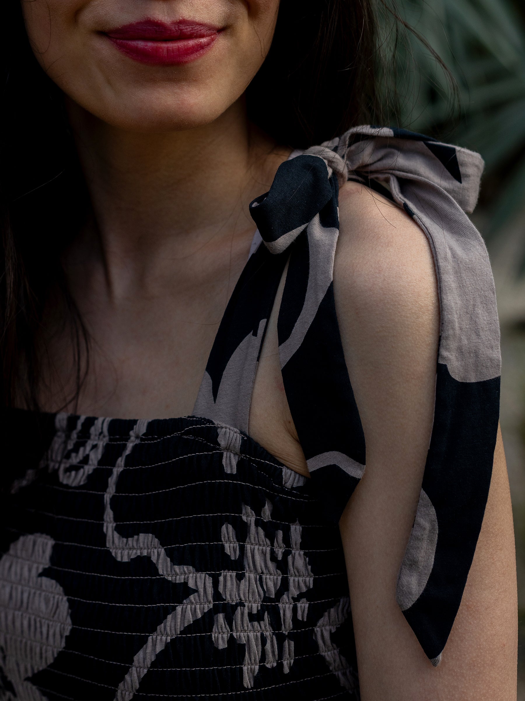 Woman in Evie Smocked Dress: black and taupe moonflower print, smocked bodice, and tied ribbon strap.