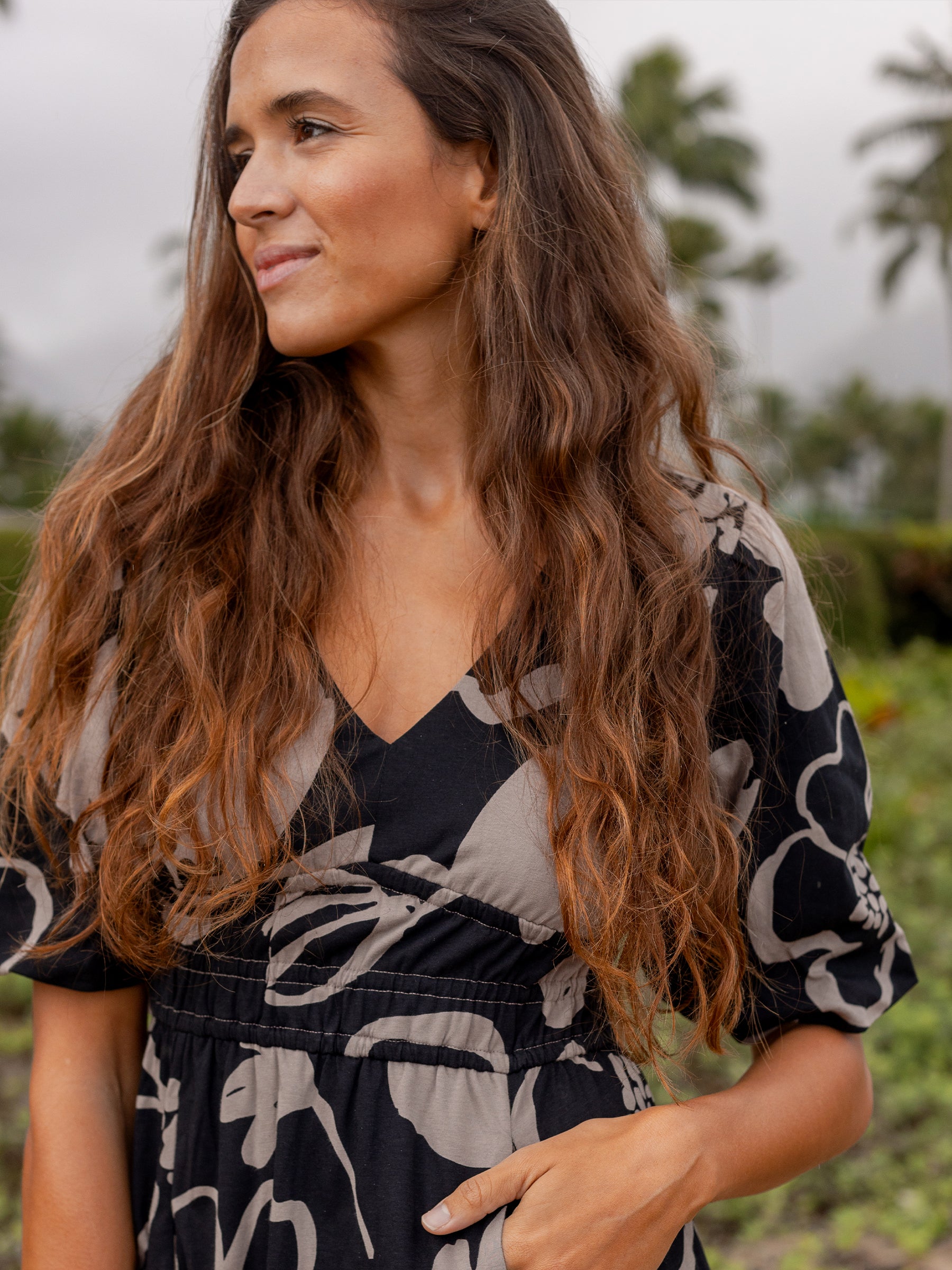 Woman in a black organic cotton Ophelia dress with taupe moonflower print, V-neck, puffed sleeves, and smocked waist.