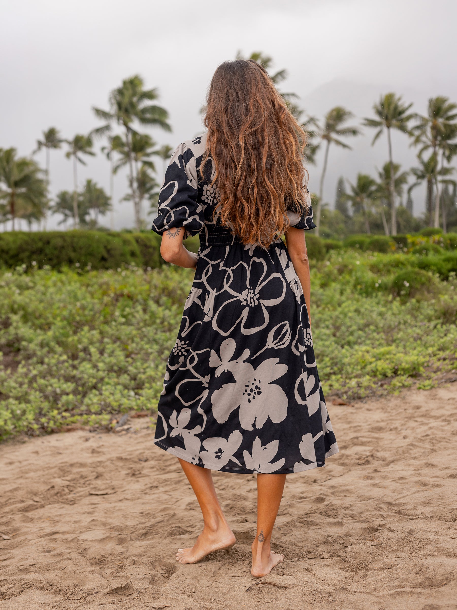 Woman in Ophelia Moonflower dress: black organic cotton midi with taupe floral print, puffed sleeves, and smocked waist.