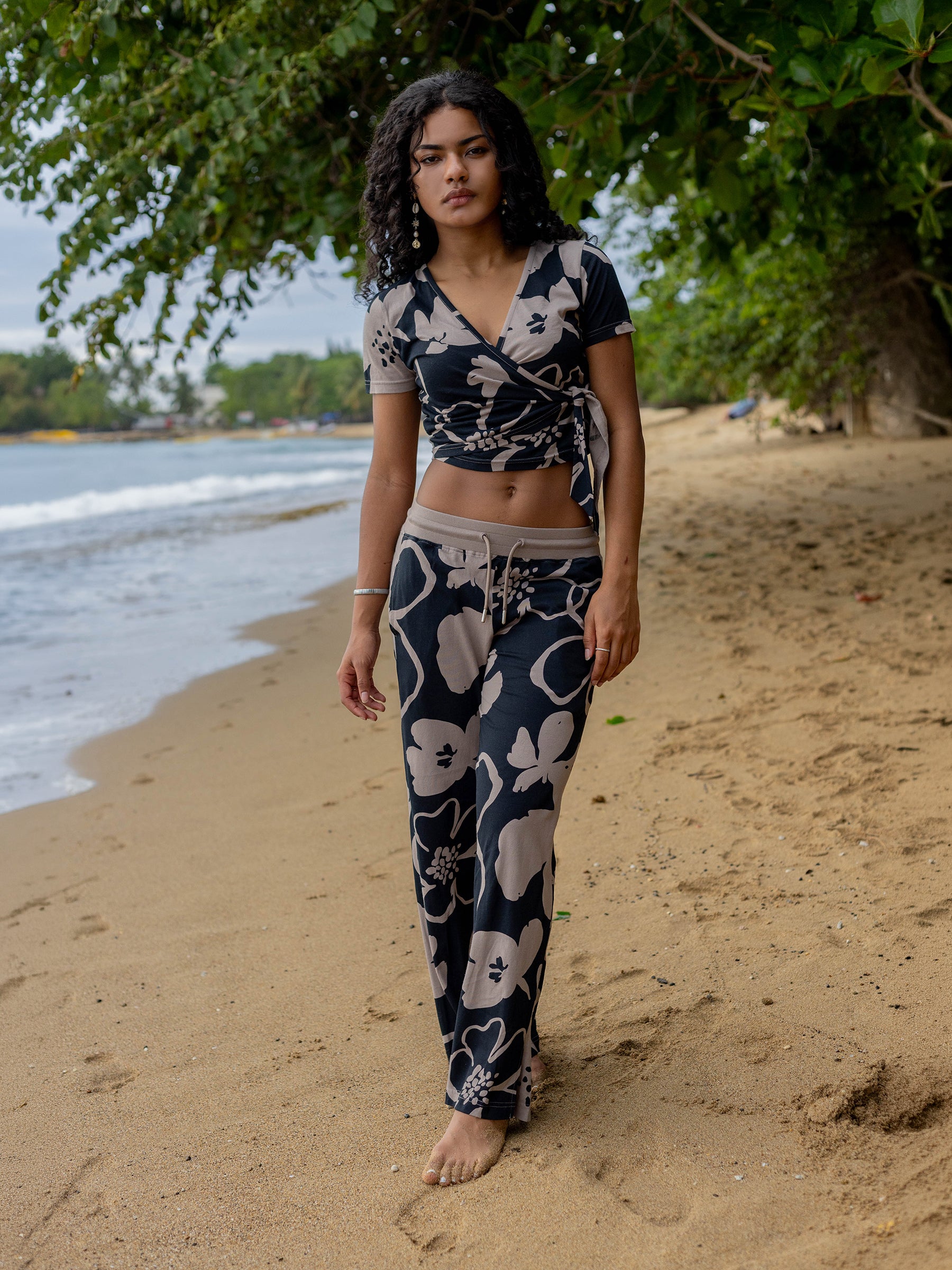 Woman in a black and taupe Moonflower wrap crop top and matching pants on a sandy beach.