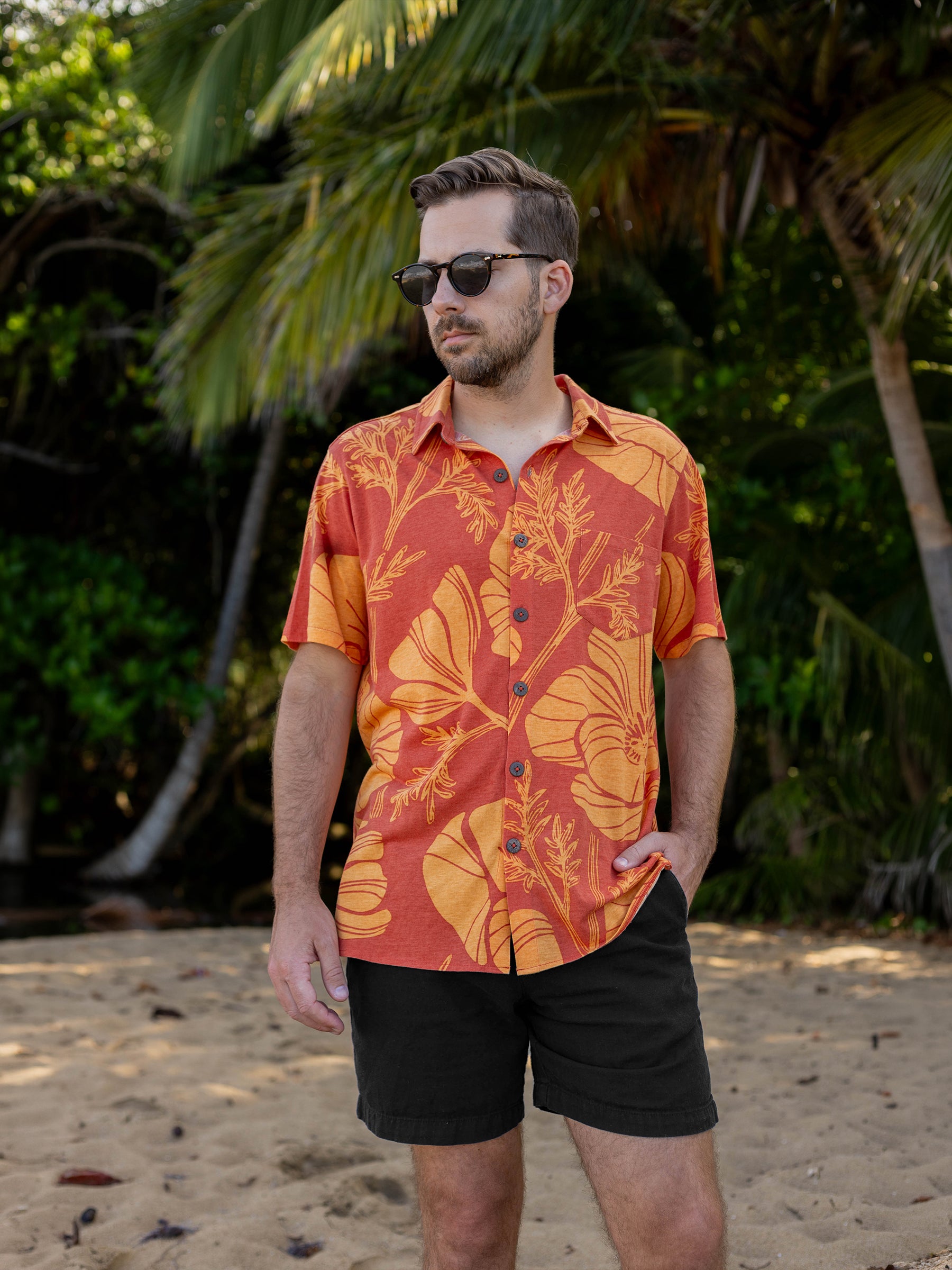 Man wearing a red and orange floral shirt with black shorts on a beach.