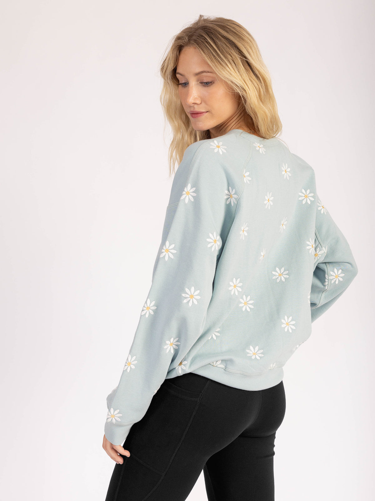 Back view of a model wearing the Daisies organic cotton sweatshirt in light blue, daisies on the back and sleeves
