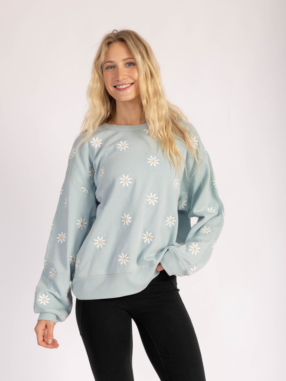 Smiling model wearing the Daisies organic cotton sweatshirt in light blue, front view