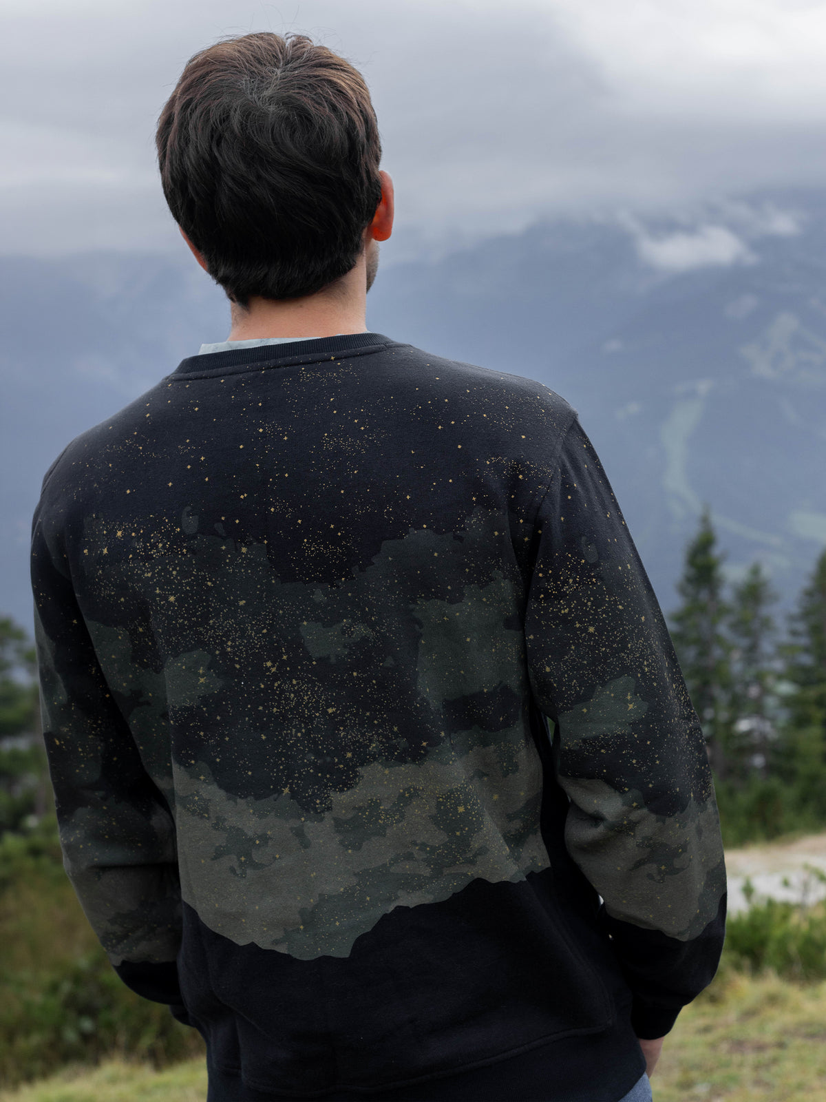 Back view of a model wearing the Embercrest organic cotton sweatshirt in front of misty mountains