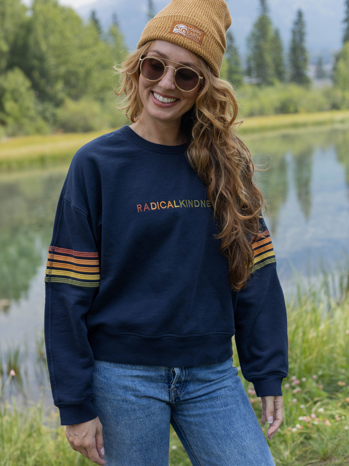 Model wearing the Radical Kindness organic cotton sweatshirt in navy with a beanie and sunglasses outdoors