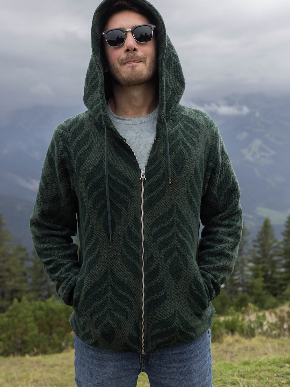Model in sunglasses wearing the forest green Verdant organic cotton sherpa zip hoodie on a mountainside