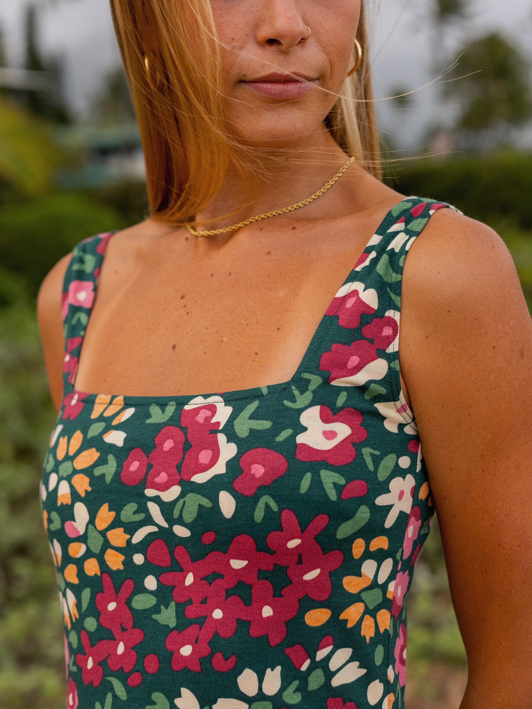 Close-up of a woman wearing a green organic cotton Lily Dress with a vibrant wildflower print, square neckline, and wide straps.