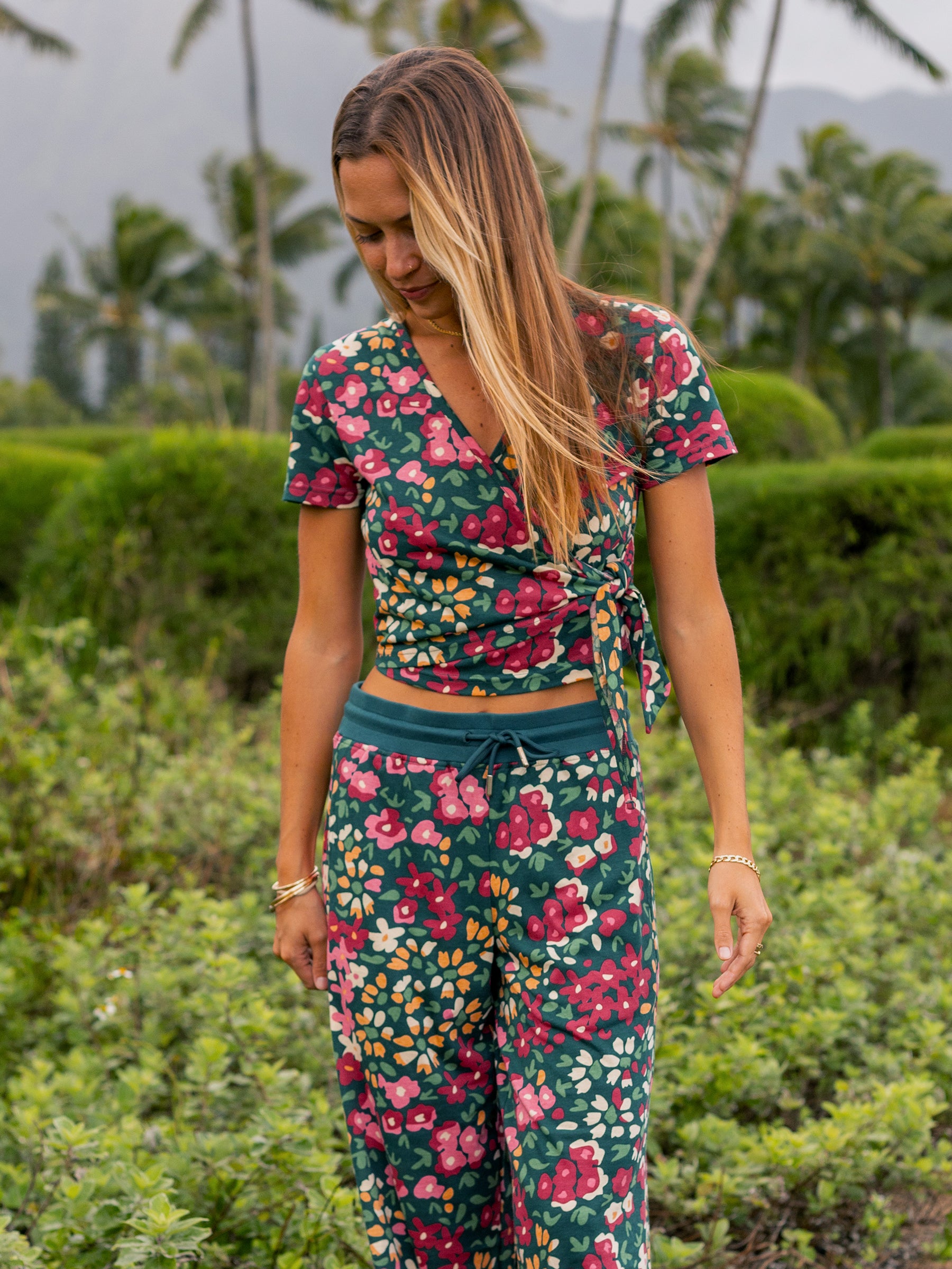 Woman in a green organic cotton wrap crop top and matching pants with a red and pink floral print.